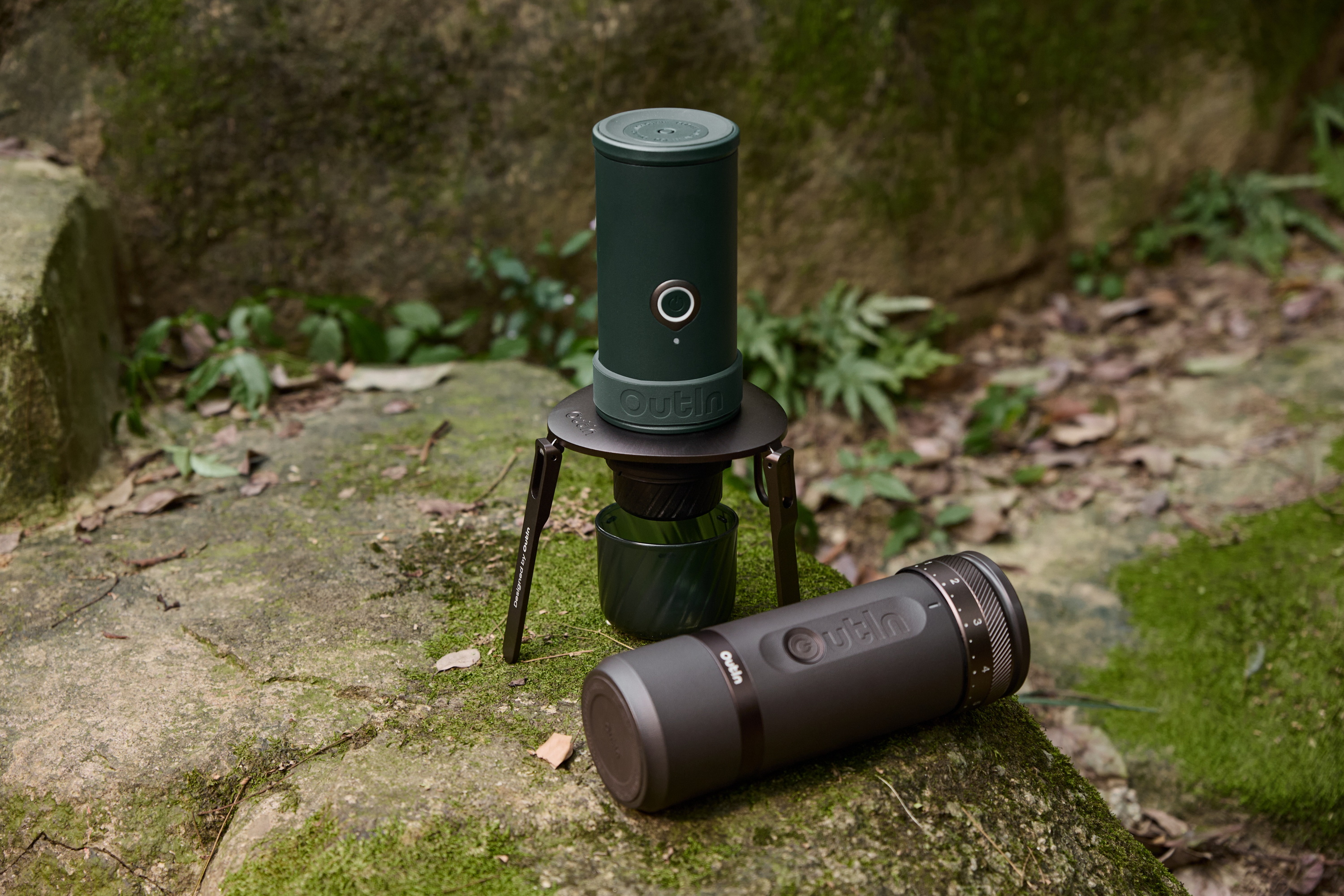 Zwei Outin-Kaffeemühlen auf moosbewachsenem Felsen im Wald.