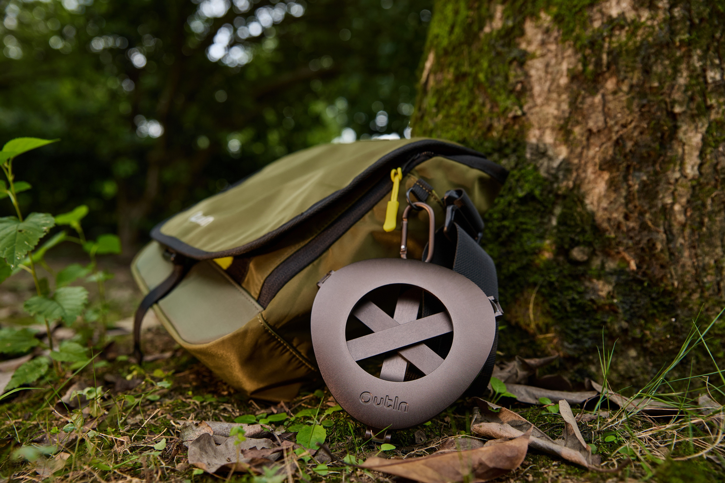 Grüne Tasche mit braunem Muster, neben Baum im Wald auf Gras.