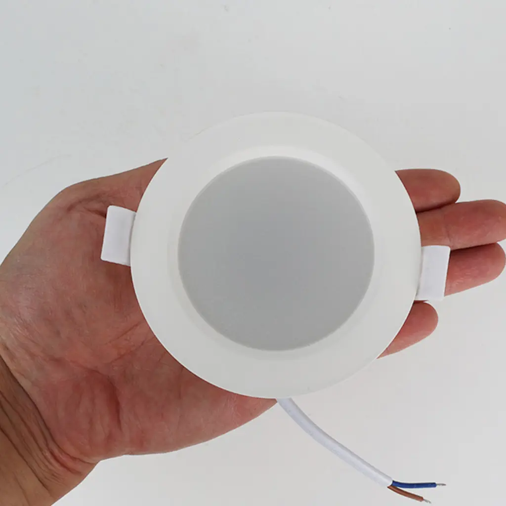 Una mano sostiene una lámpara empotrada blanca con cables.