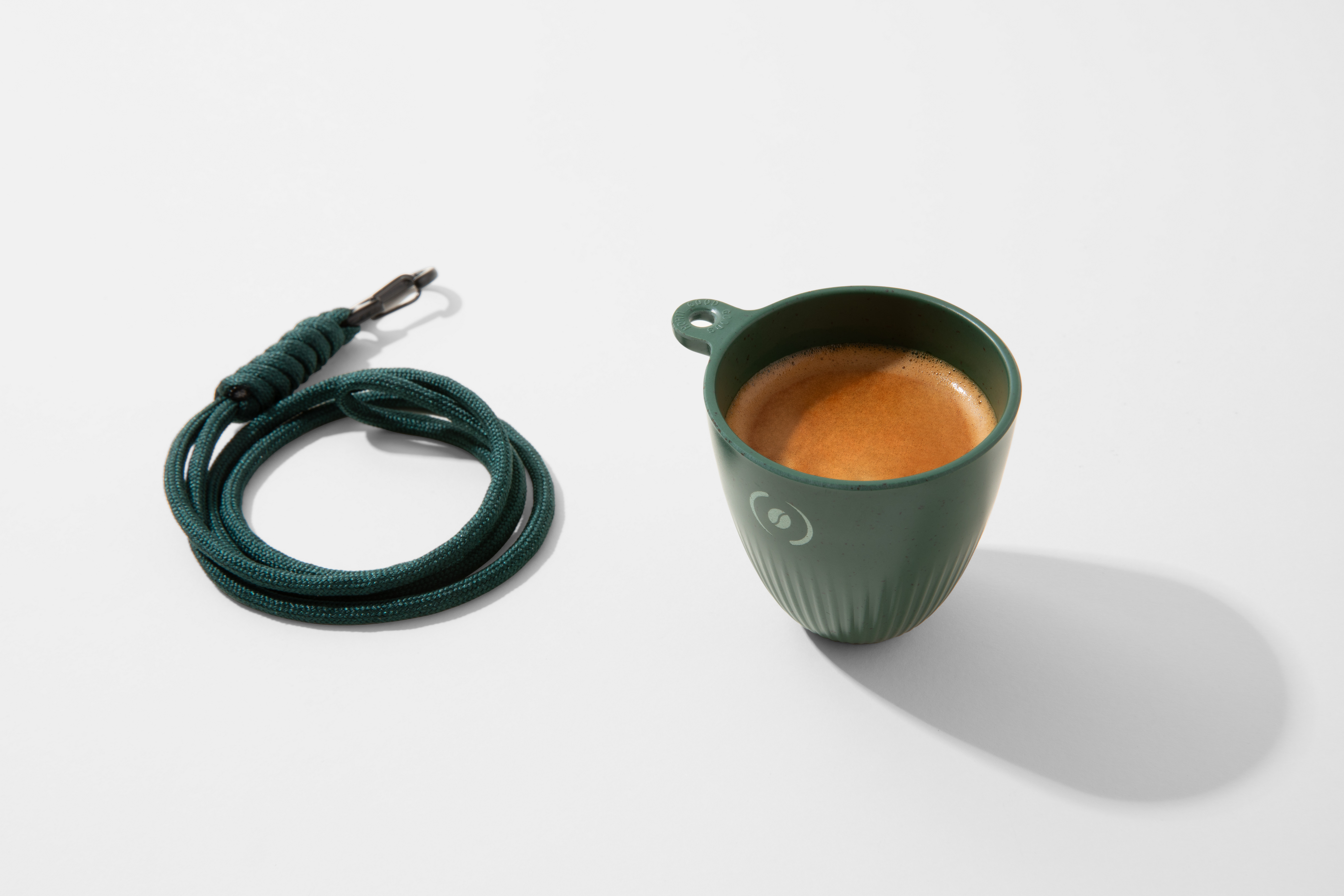 Una tazzina verde da shot con espresso accanto a una corda verde con clip.