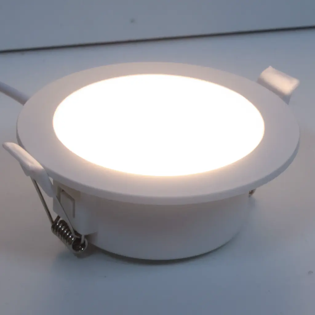 Una luz empotrada blanca con clips de resorte y un cable sobre una superficie blanca.