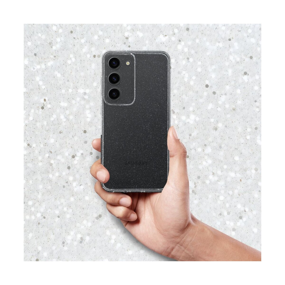 Una mano tiene uno smartphone nero con tre fotocamere su sfondo scintillante.