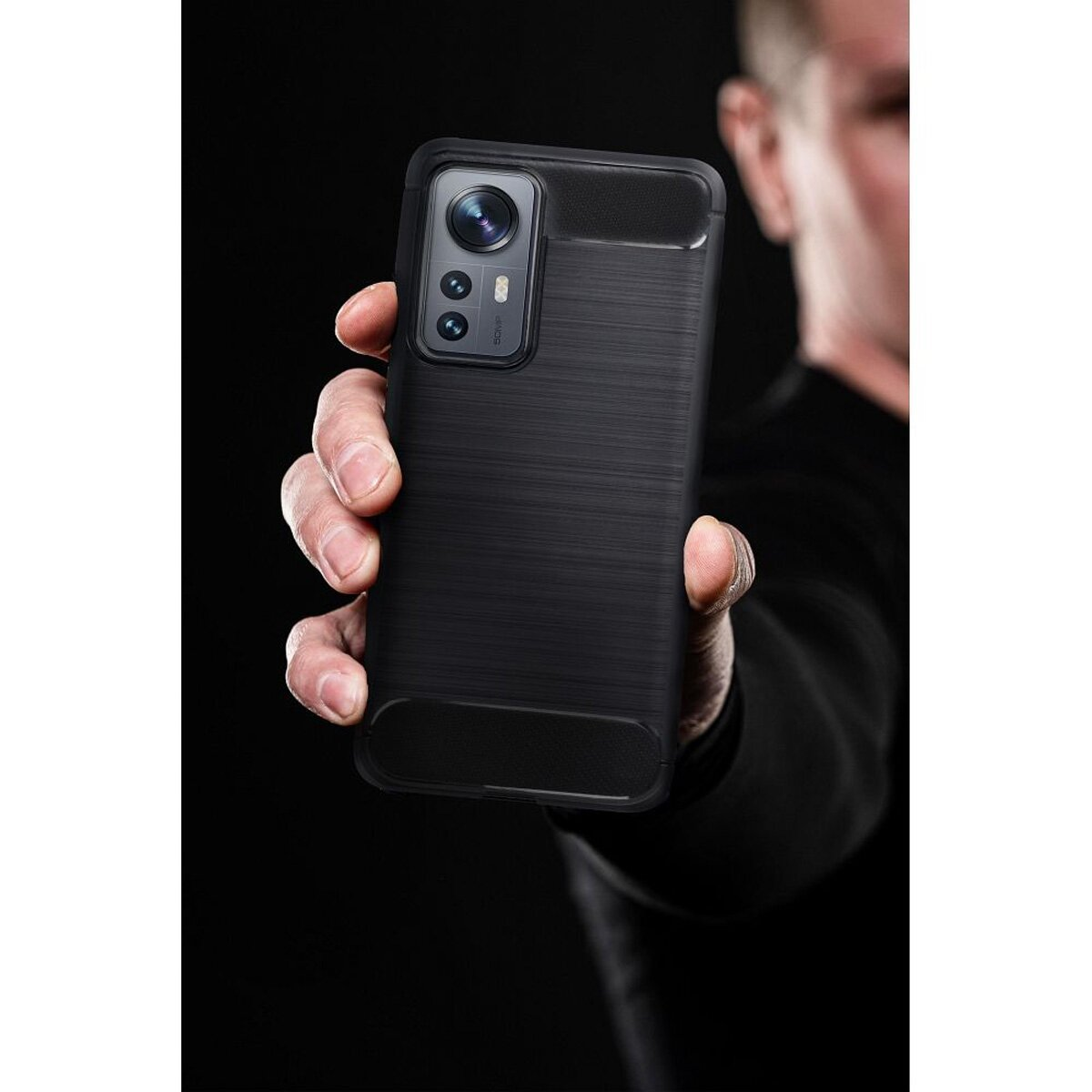 Ein Mann hält ein schwarzes Handy mit dreifacher Kamera und gebürsteter Textur.