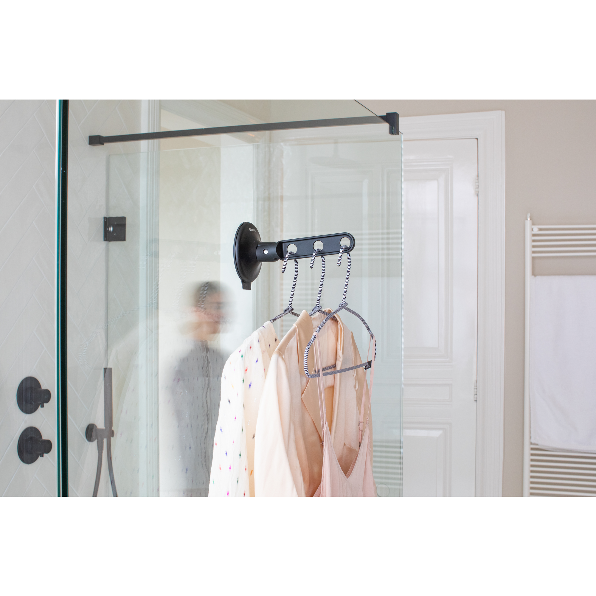 Black and white hangers with clothes on a shower wall in a bathroom.