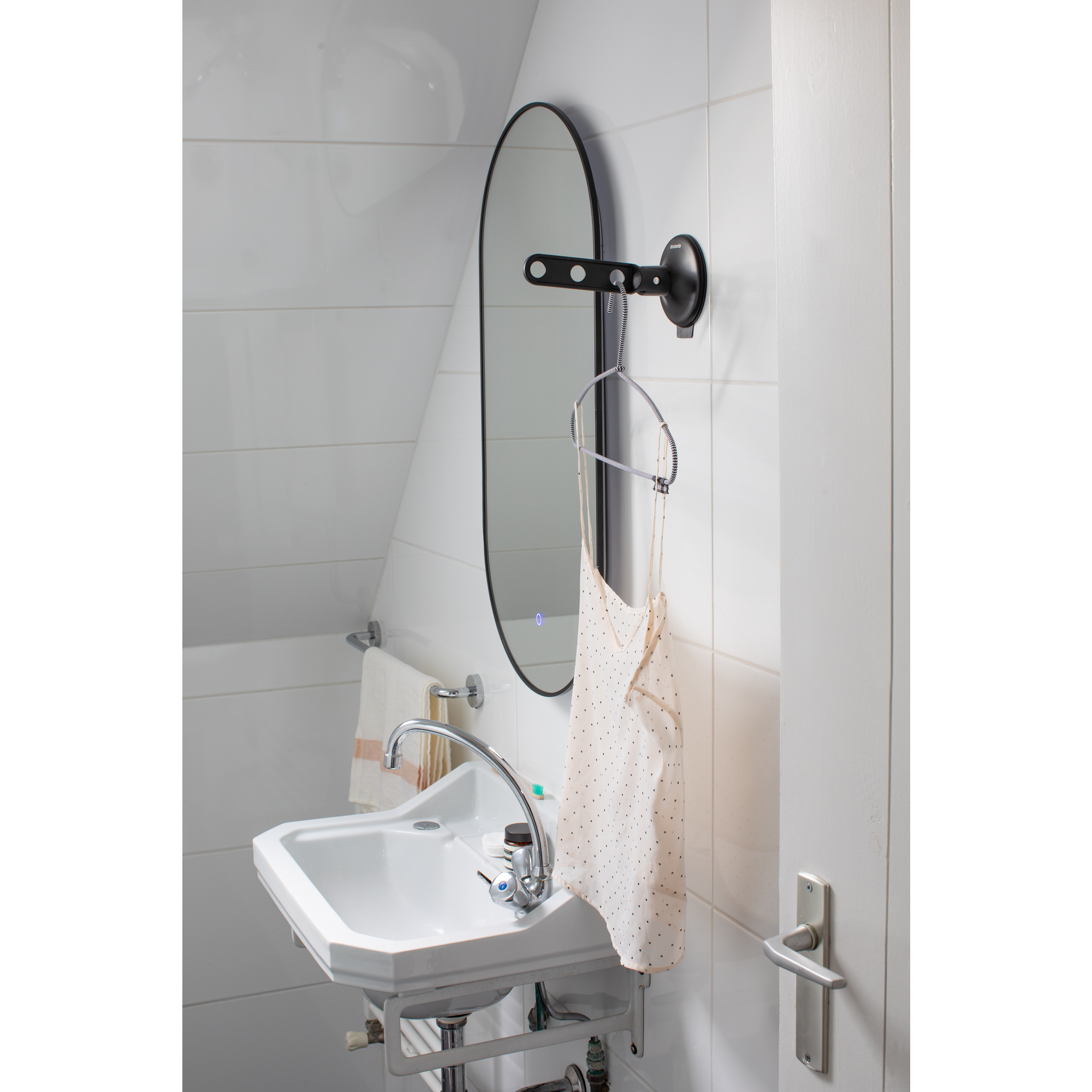 A bathroom with a sink, mirror, towel, and a dress on a hanger.
