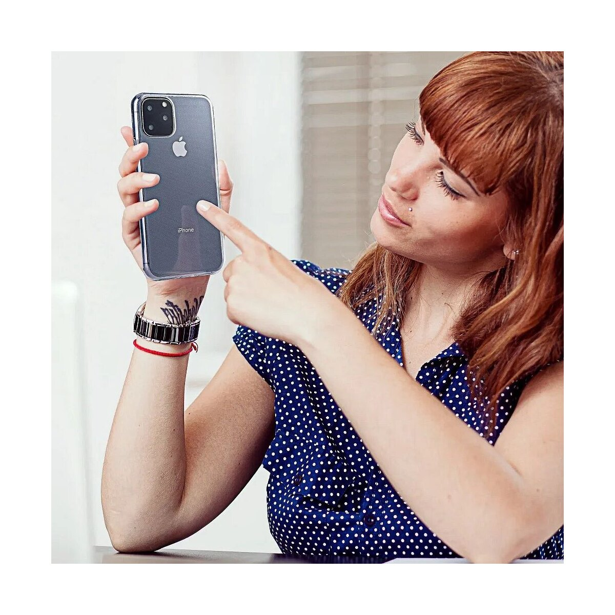 Een vrouw met rood haar houdt een iPhone vast en wijst ernaar.