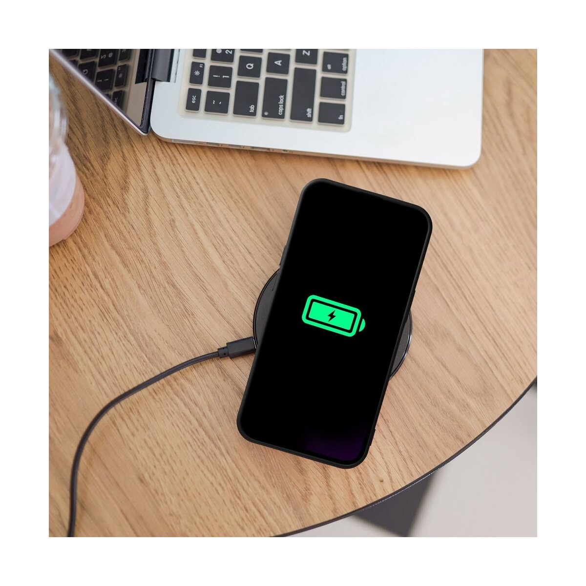 Ein Smartphone lädt auf einer kabellosen Ladestation neben einem Laptop.
