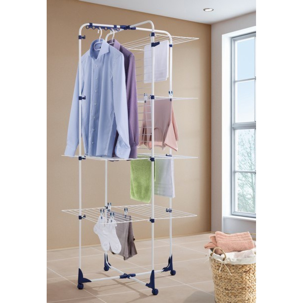 Biały stojak na pranie z ubraniami i ręcznikami, obok kosza.