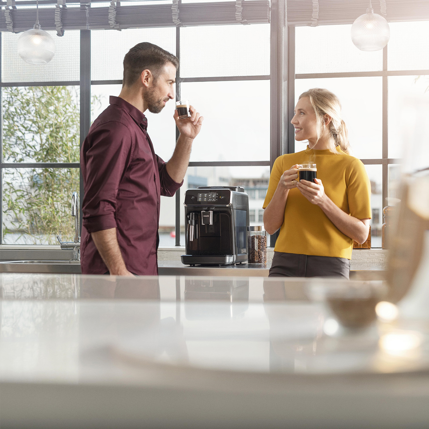 Pareja disfrutando café junto a la ventana con cafetera.
