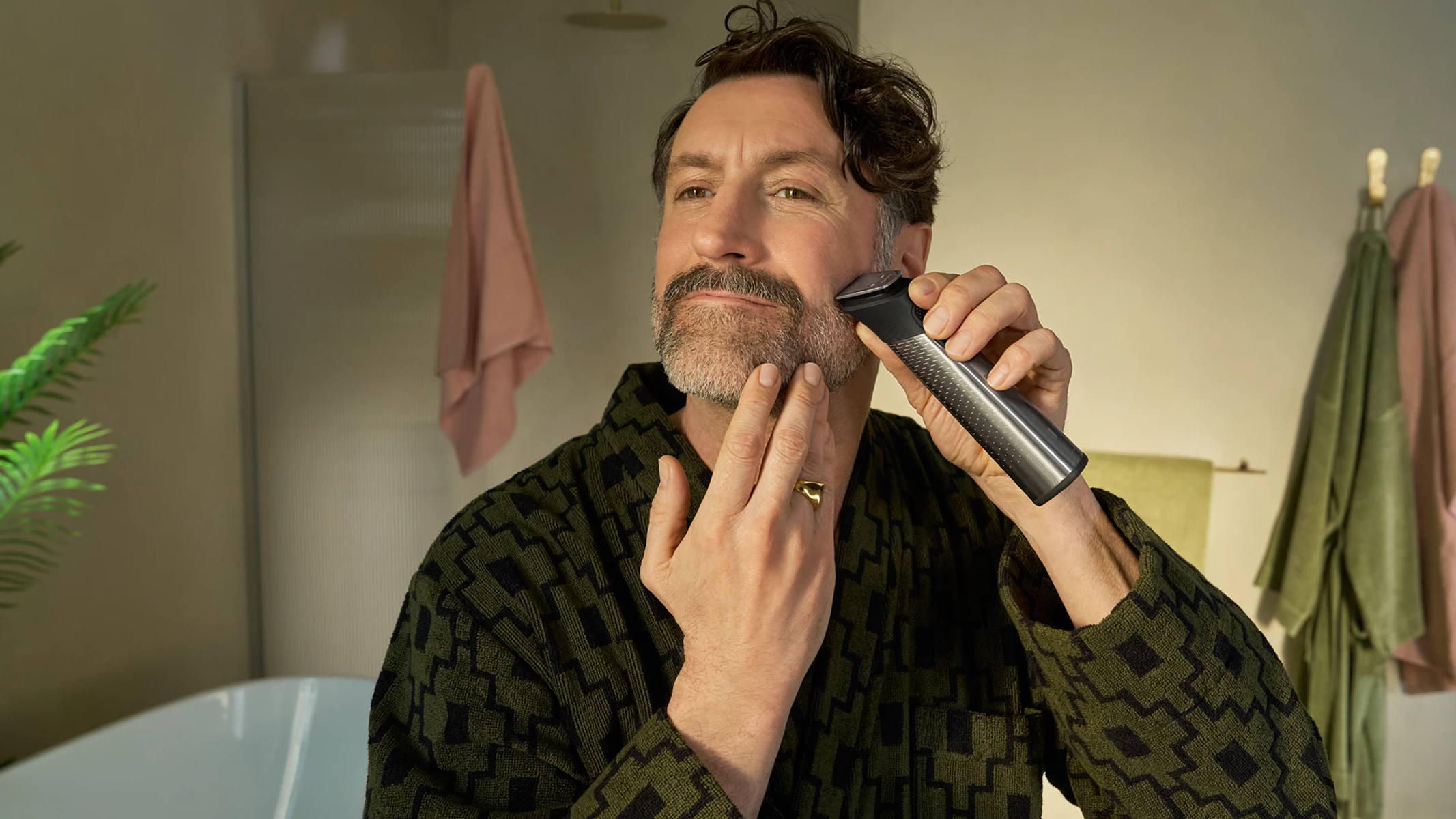 Mann im Bademantel rasiert sich mit Trimmer im Bad.