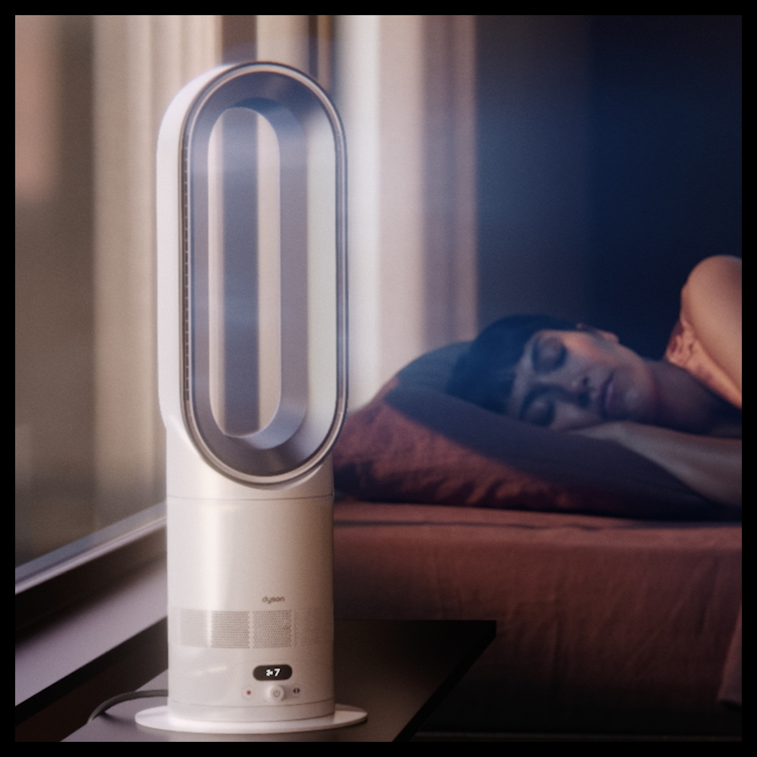 Un ventilatore Dyson bianco accanto a una persona che dorme nel letto.