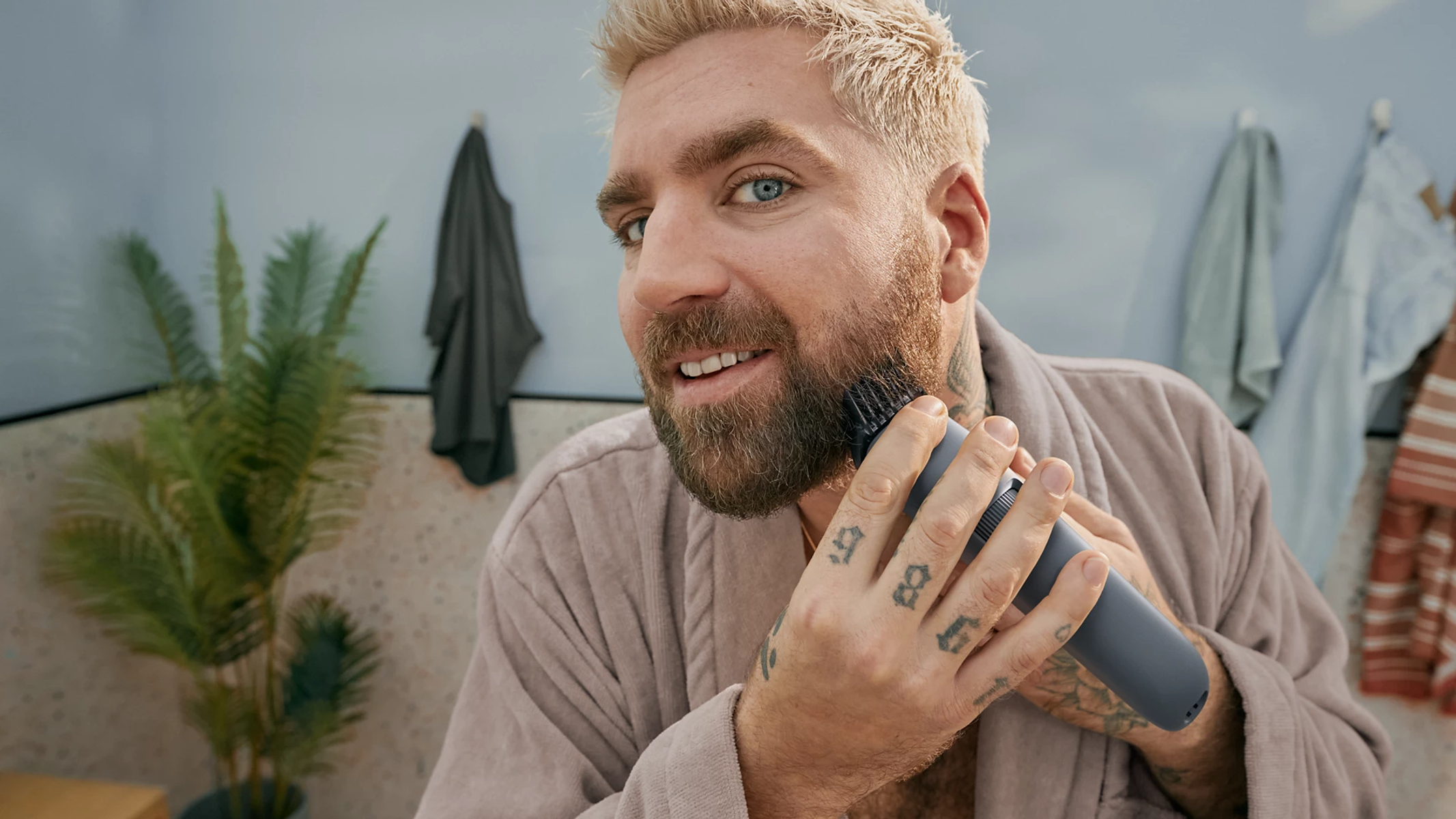 Man with beard trimmer in bathroom, in front of mirror, with plants.