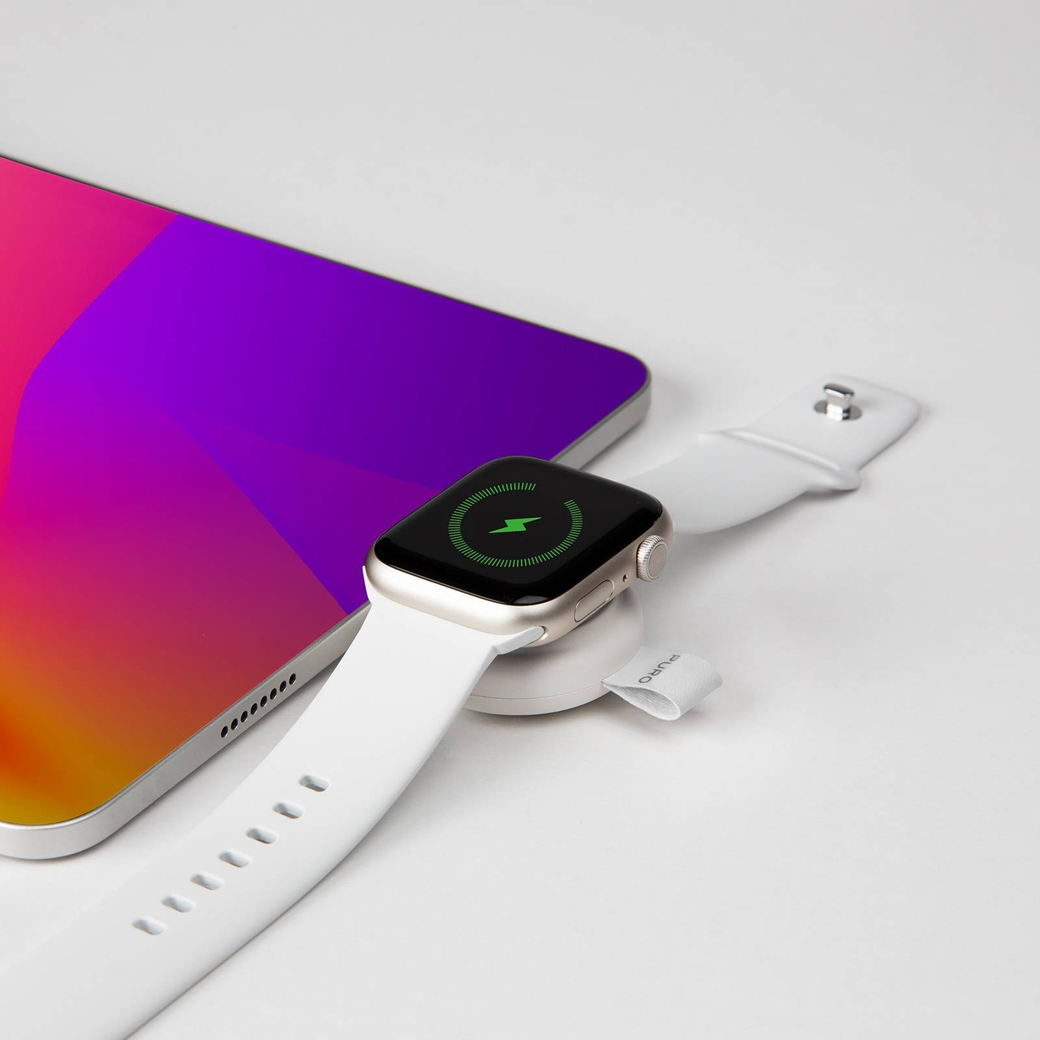 Un smartwatch plateado cargando en un muelle blanco junto a una tableta degradada.