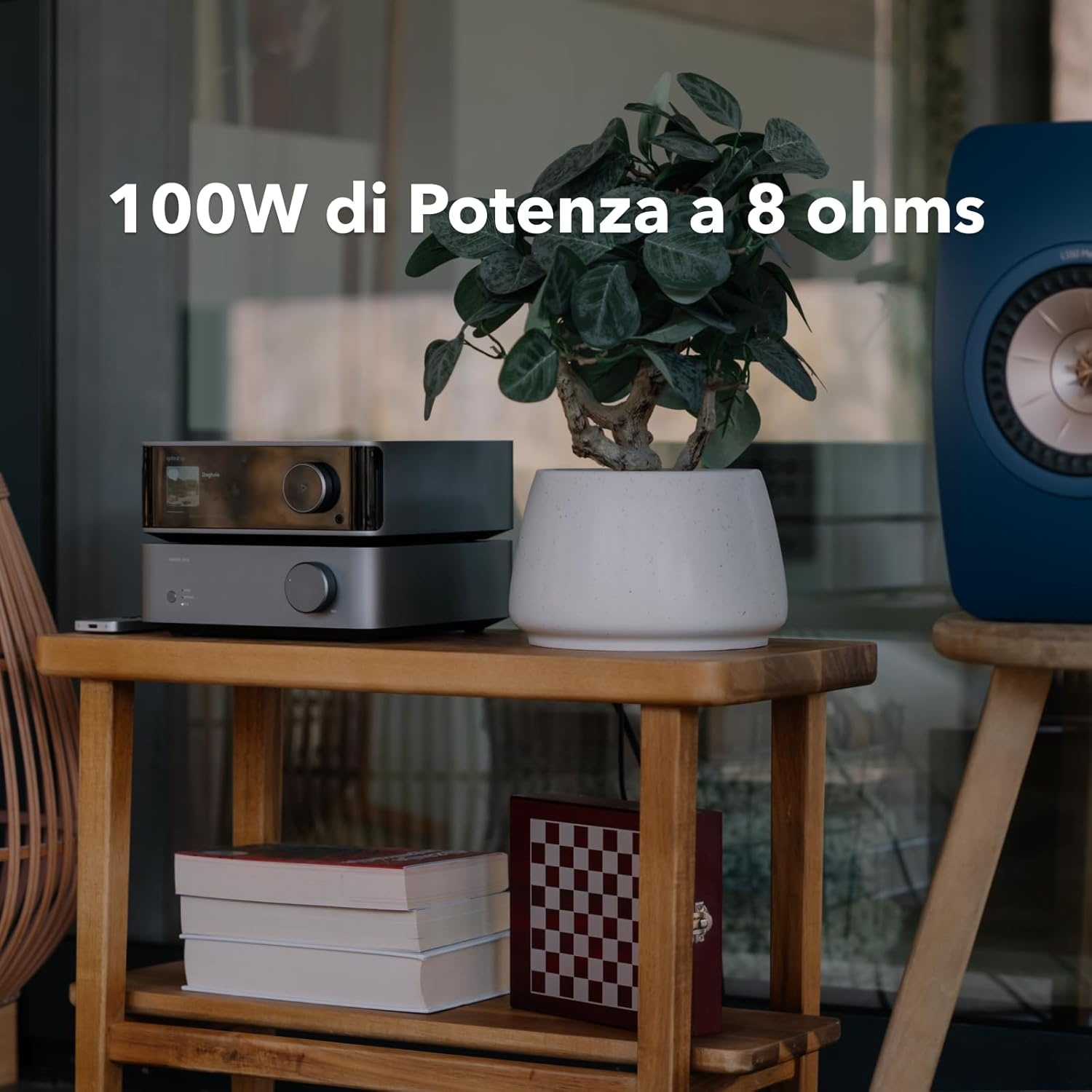 Twee zilveren audioapparaten op een houten plank, naast een potplant en een blauwe luidspreker.