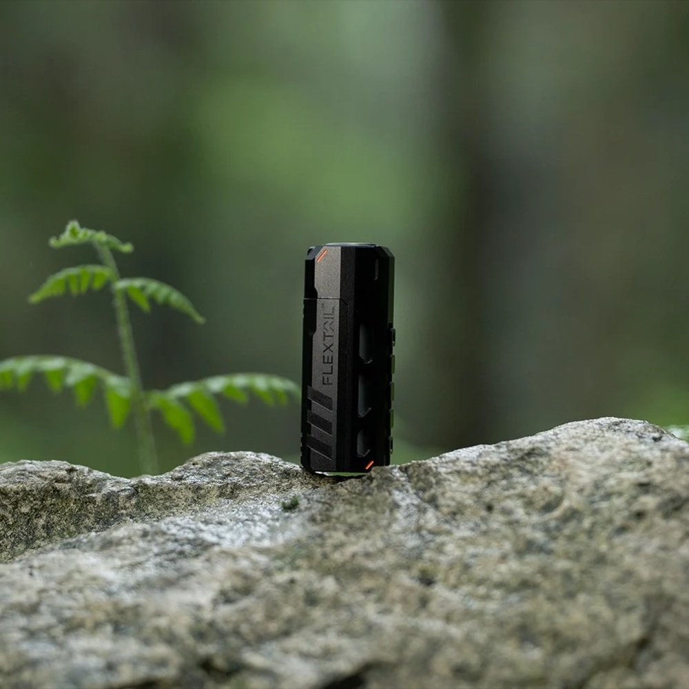 Ein schwarzes, zylindrisches Gerät mit orangen Akzenten ruht auf einem Stein.