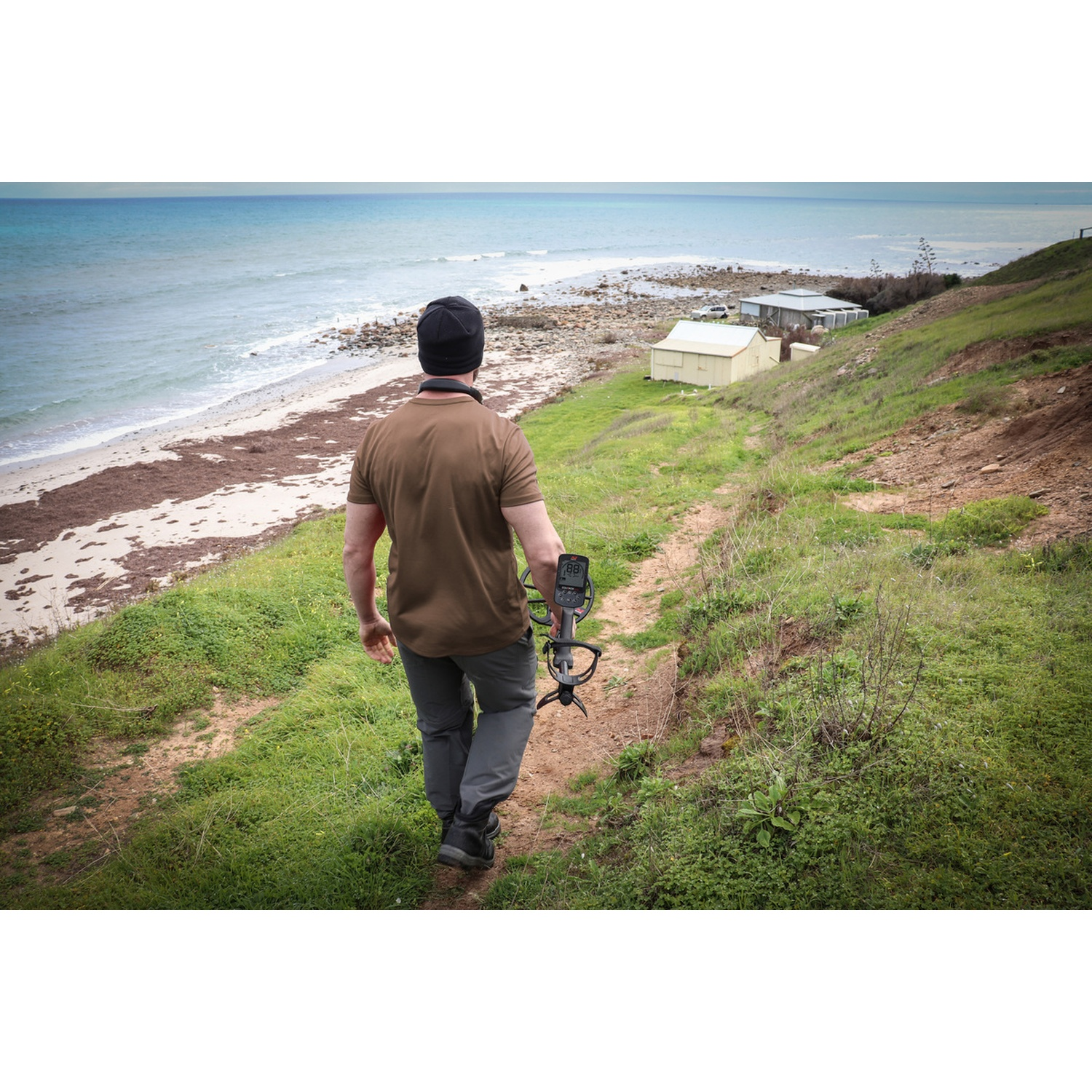 Uomo con metal detector cammina sul sentiero della spiaggia verso il mare.