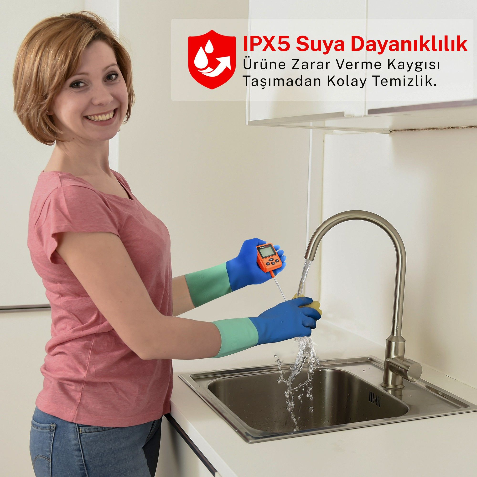 Mavi ve yeşil eldivenli bir kadın, akan suyuyla dijital termometreyi temizliyor.
