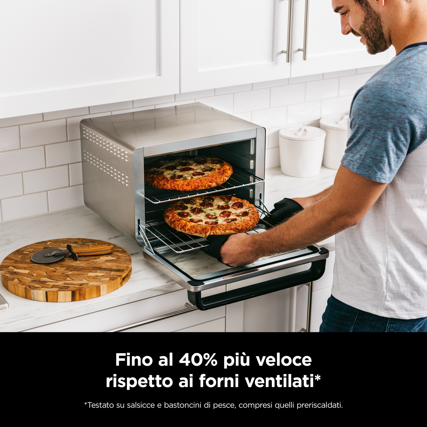 Mann nimmt zwei Pizzen aus einem Toaster-Ofen, der auf einer Küchentheke steht.