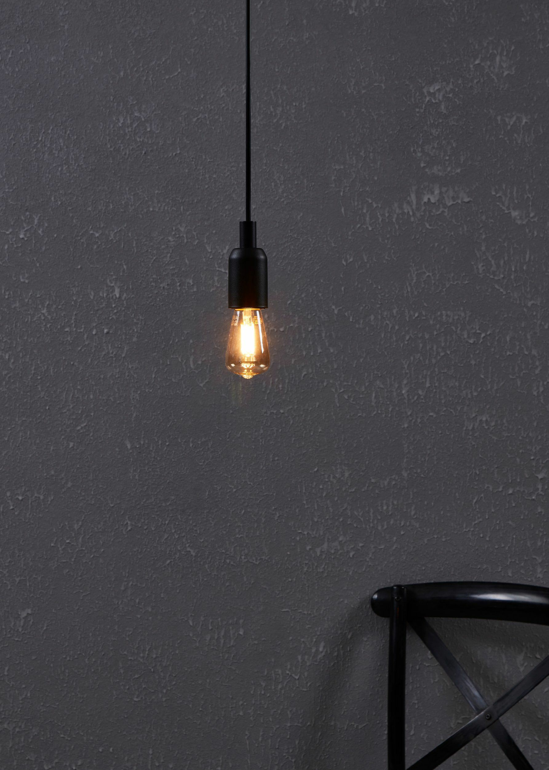 Une ampoule Edison allumée pend à un fil noir devant un mur gris texturé.
