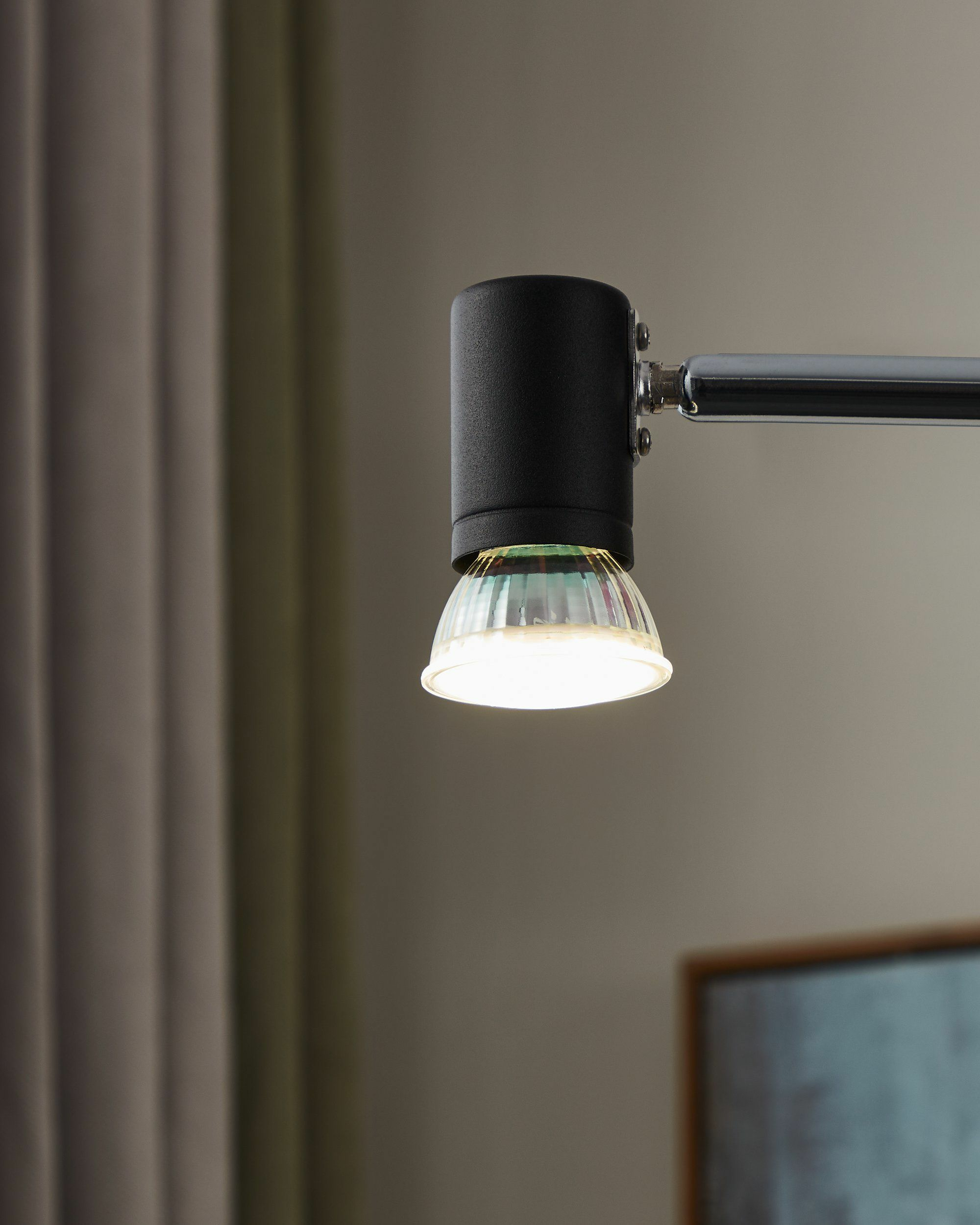Un braccio di lampada nero con diffusore in vetro e lampadina accesa.