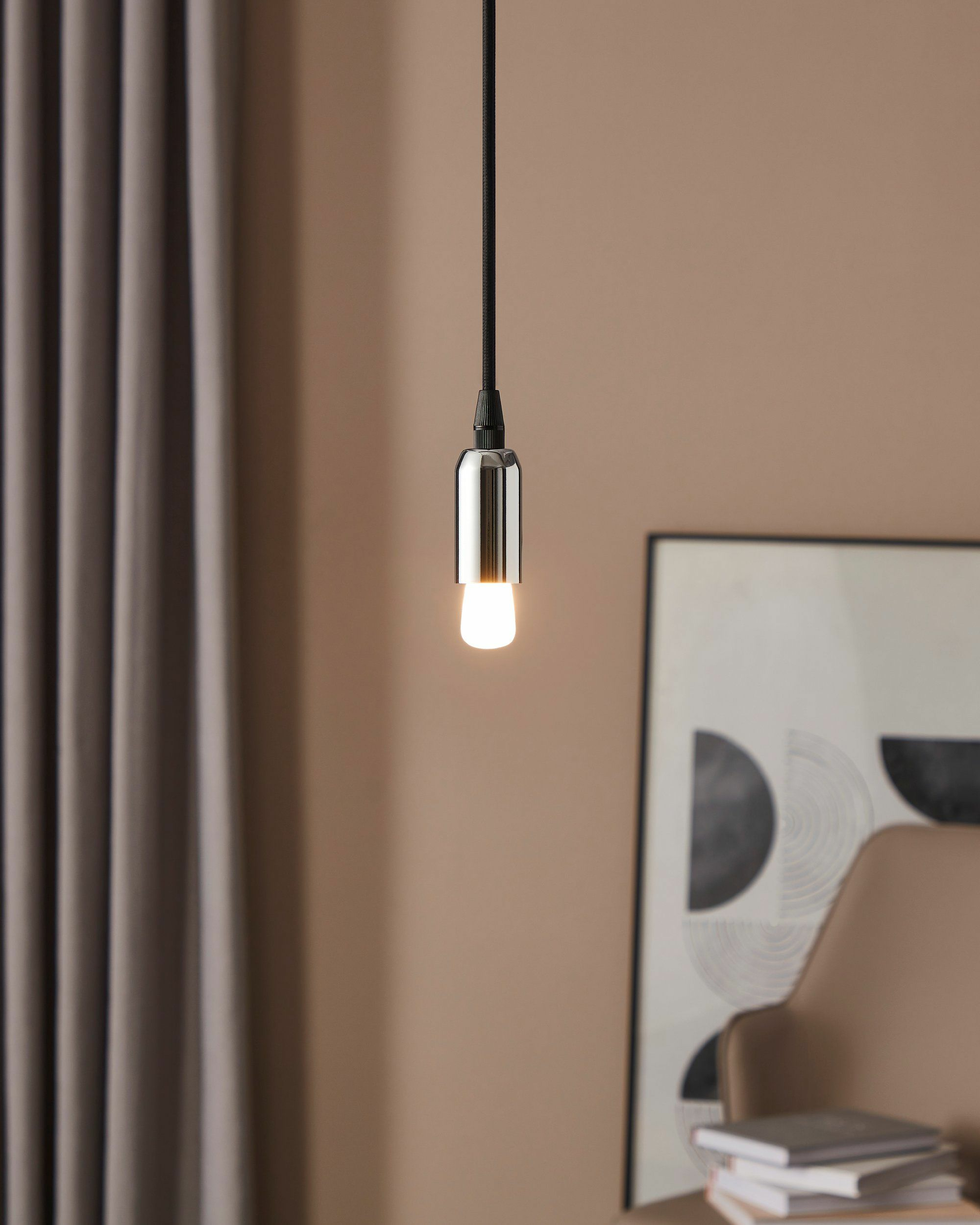 Une lampe suspendue avec un boîtier argenté au-dessus d'une pile de livres.