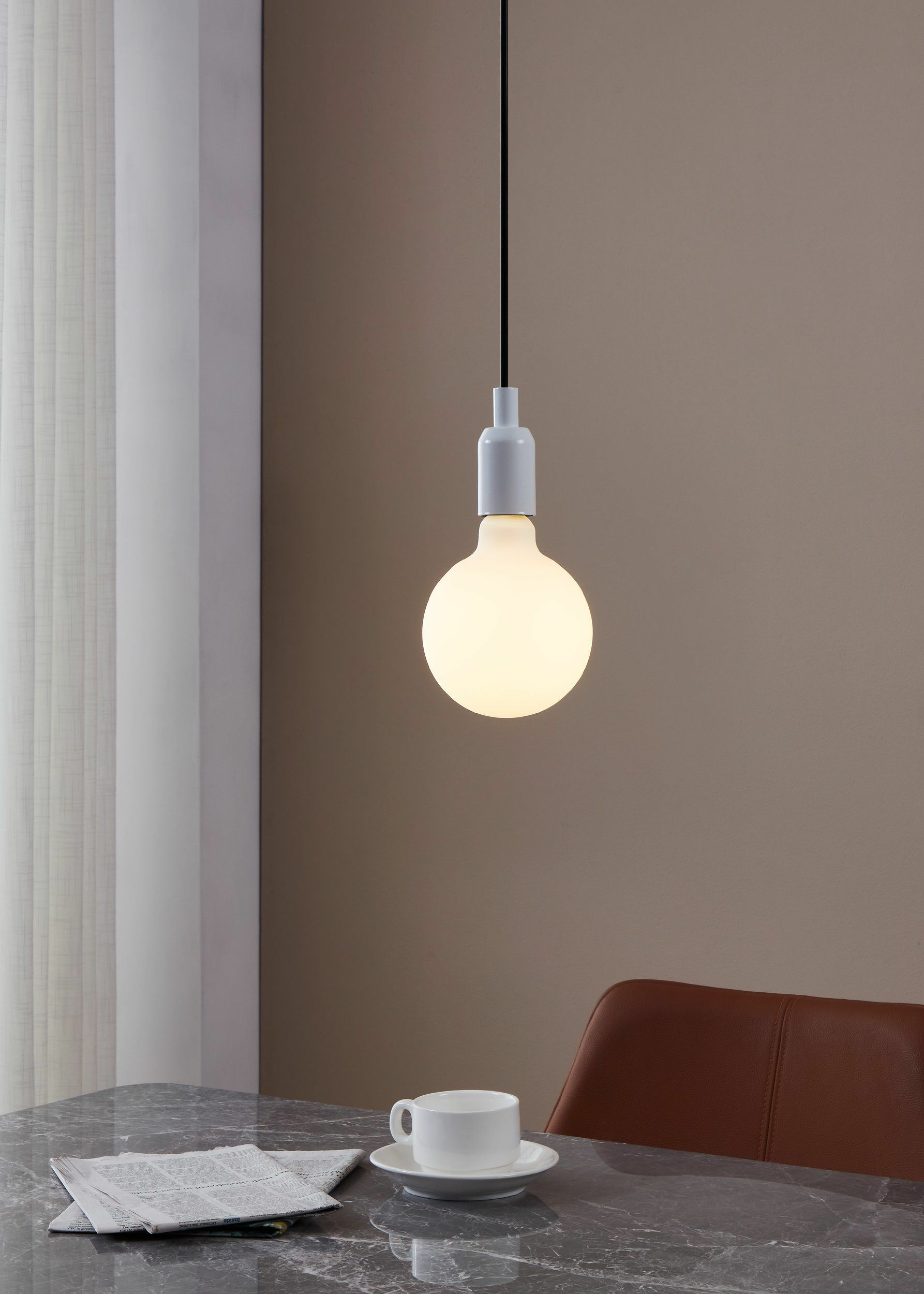 Une ampoule blanche suspendue au-dessus d'une table en marbre avec journal et tasse.