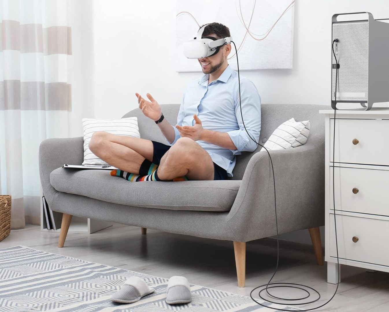 Hombre con gafas VR en sofá, calcetines coloridos, cable a PC.