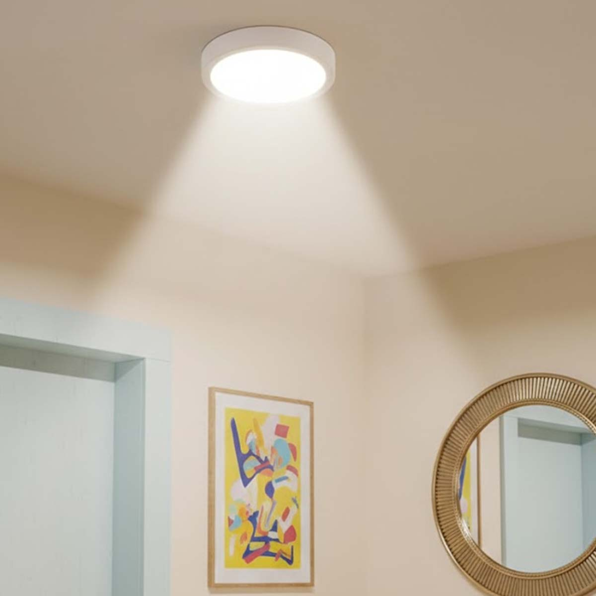 Una luz de techo blanca ilumina una pared con un espejo redondo y un cuadro.