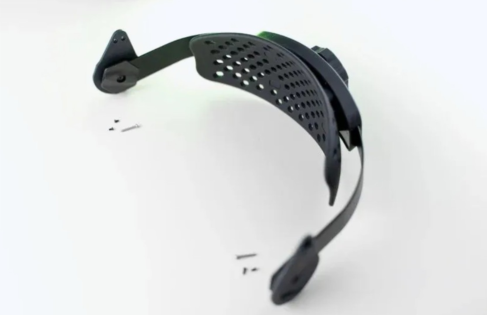 Un visor protector negro con orificios de ventilación y tornillos sobre fondo blanco.