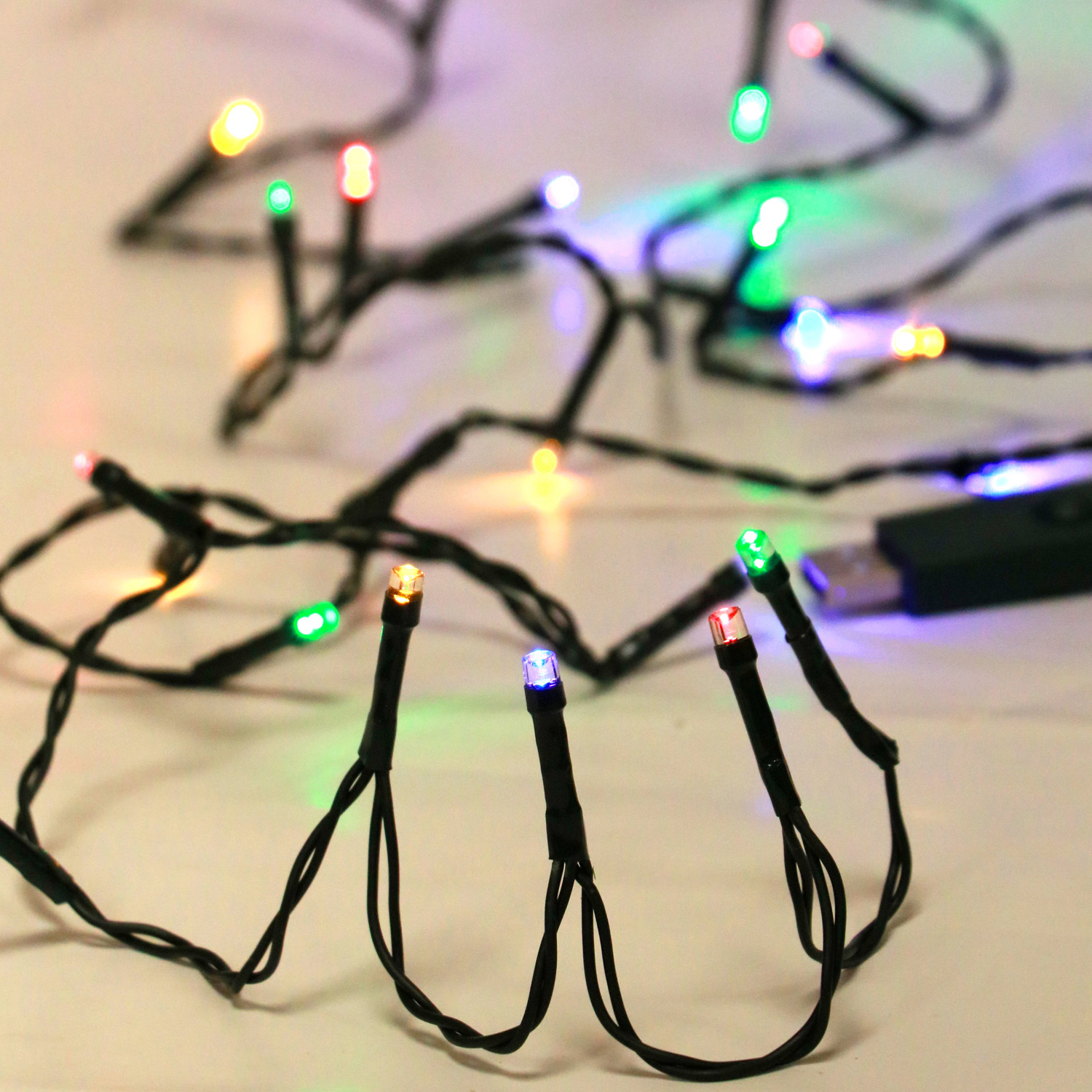 Una stringa di luci LED colorate, per lo più verdi, blu e rosse, su superficie bianca.