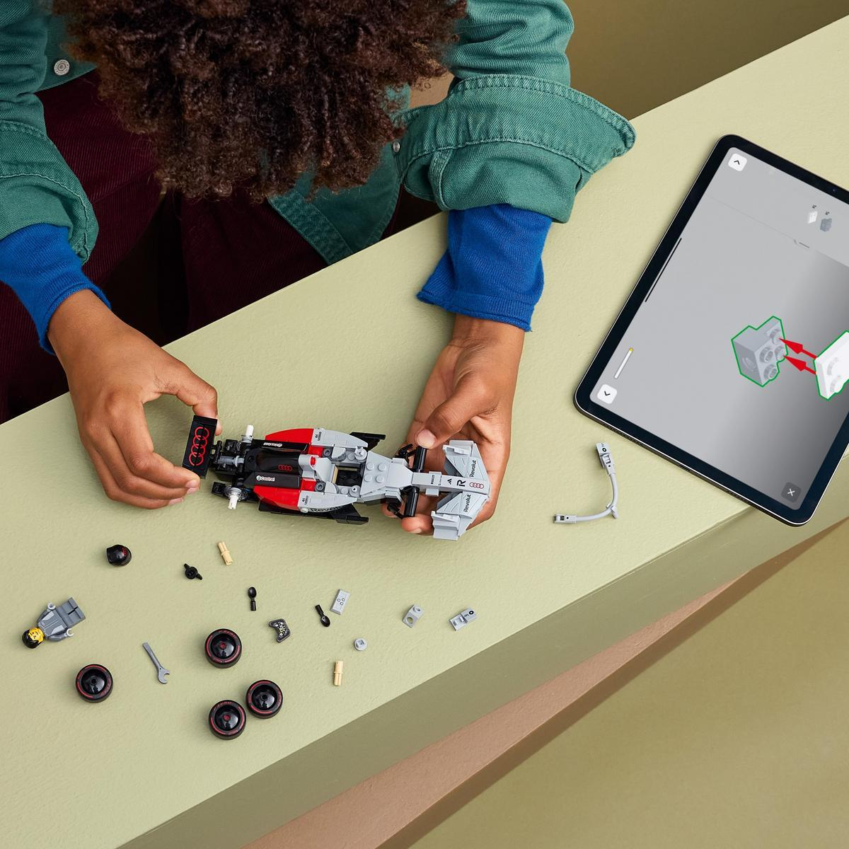 Un bambino costruisce un'auto Lego grigia e rossa su un tavolo, con un tablet nelle vicinanze.