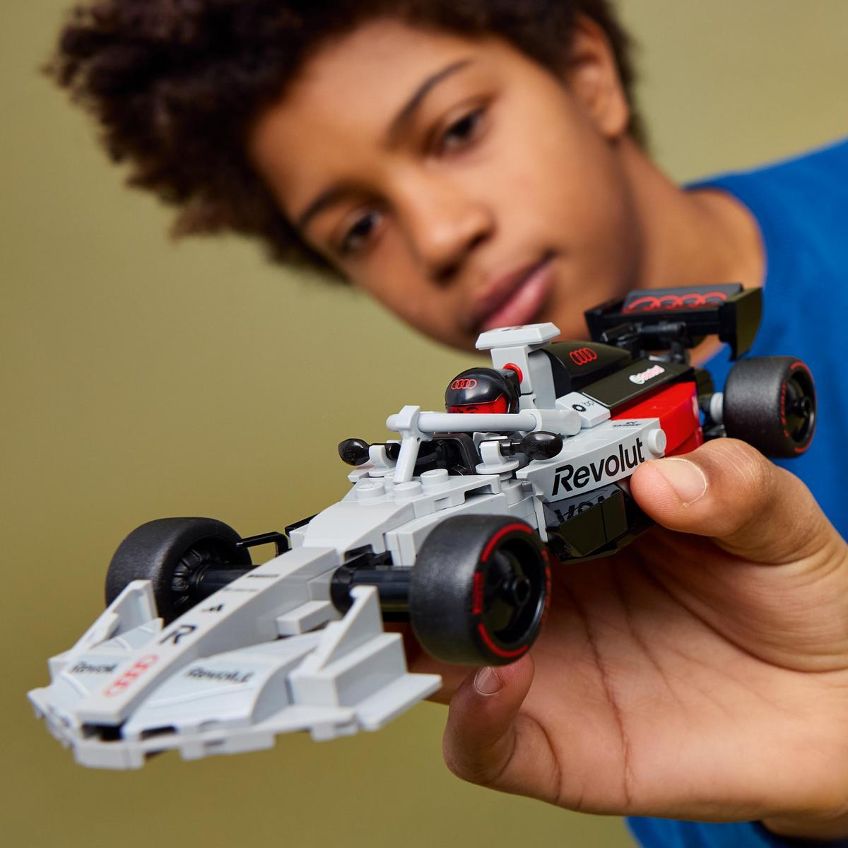 Un ragazzo tiene un'auto da corsa Lego grigia e rossa con marchio Audi.