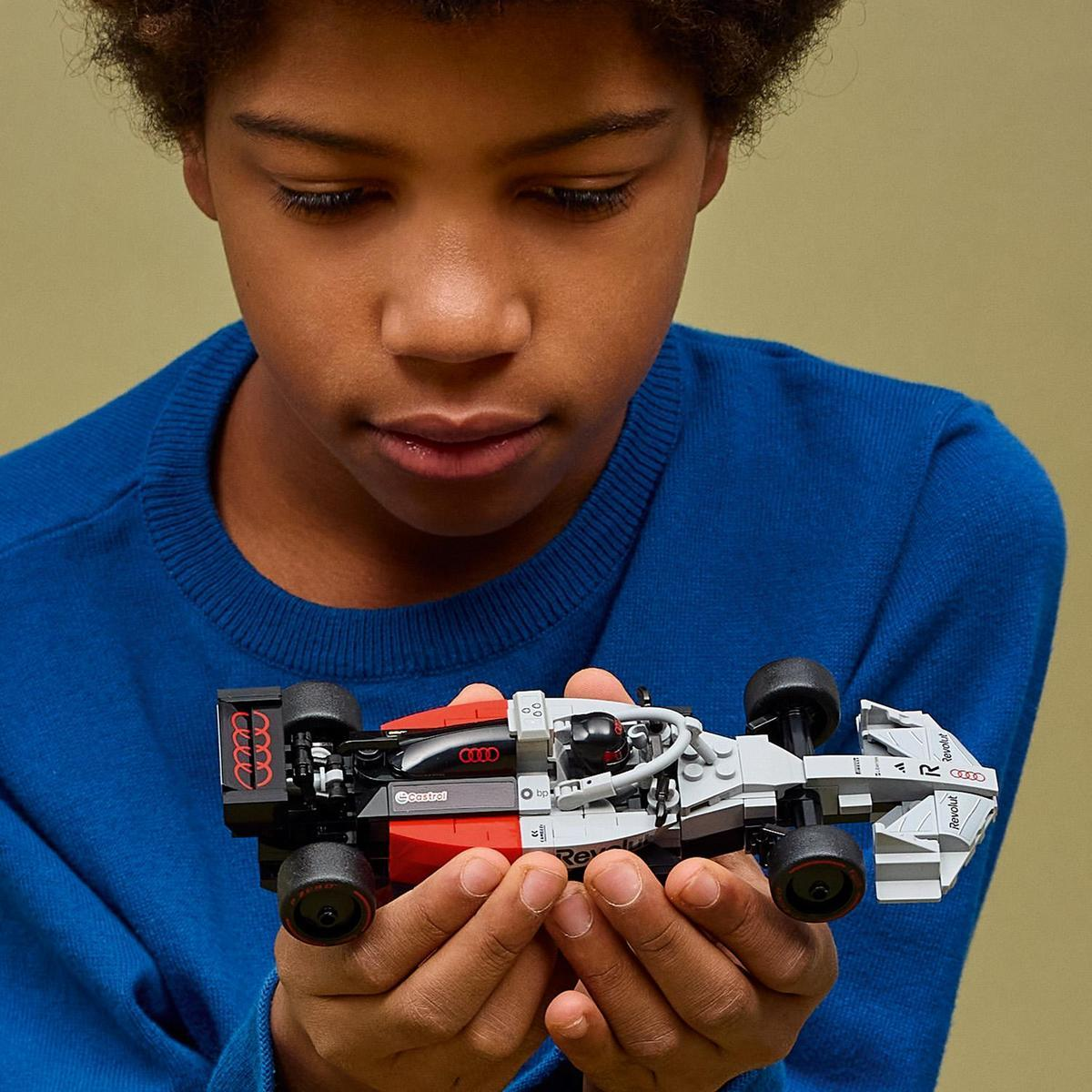 Un ragazzo tiene in mano un'auto da corsa Lego. L'auto è rossa, grigia e nera.