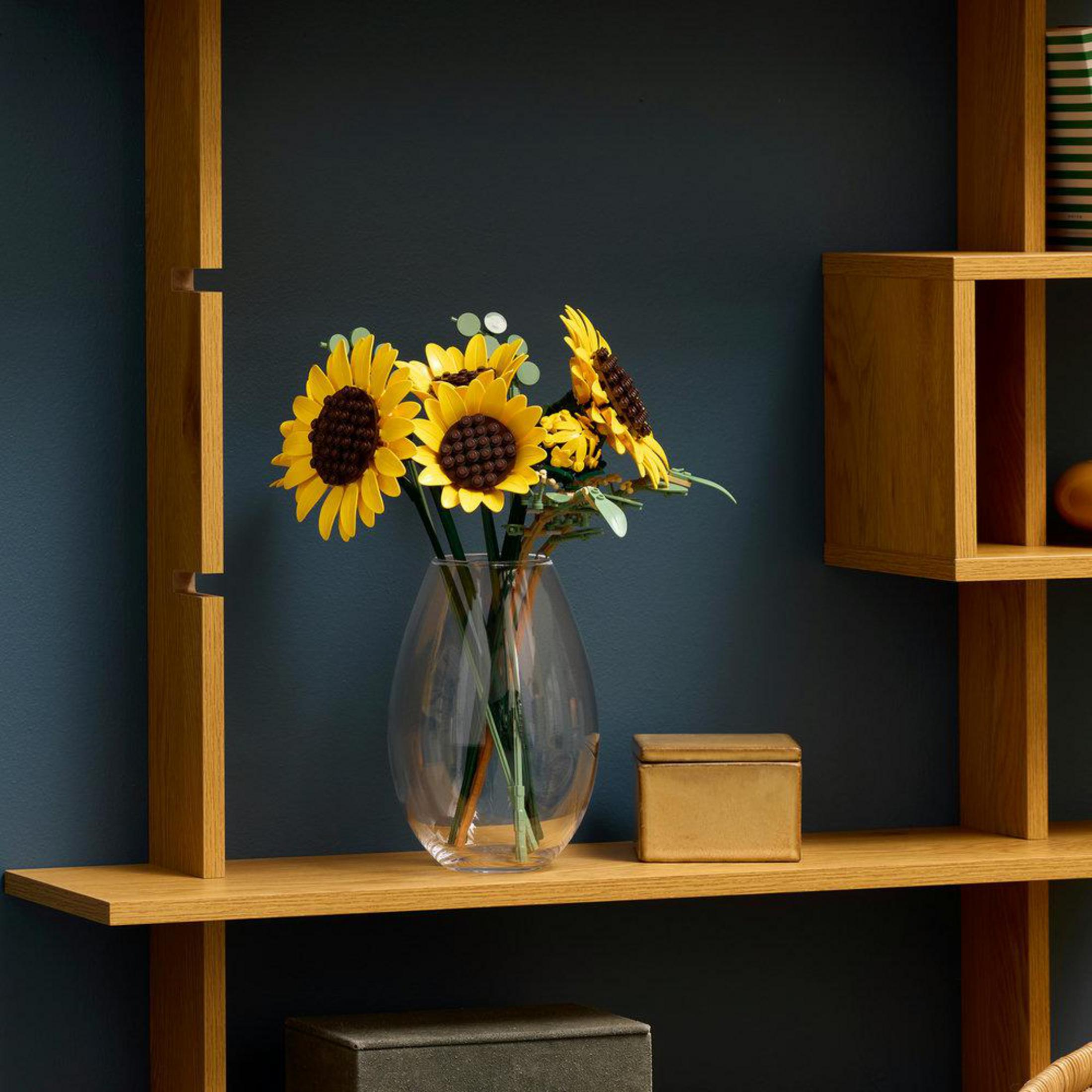 Słoneczniki w szklanym wazonie na drewnianej półce na ciemnoniebieskiej ścianie.
