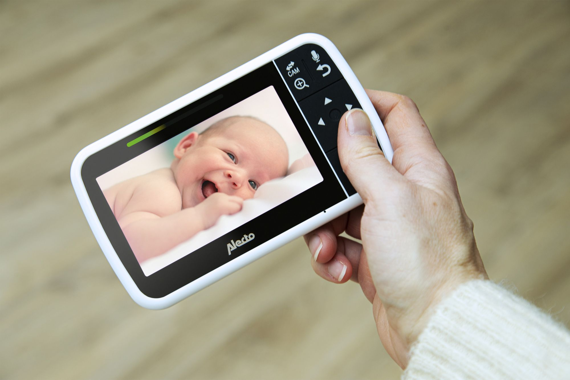 Hand holding baby monitor showing smiling baby on screen.