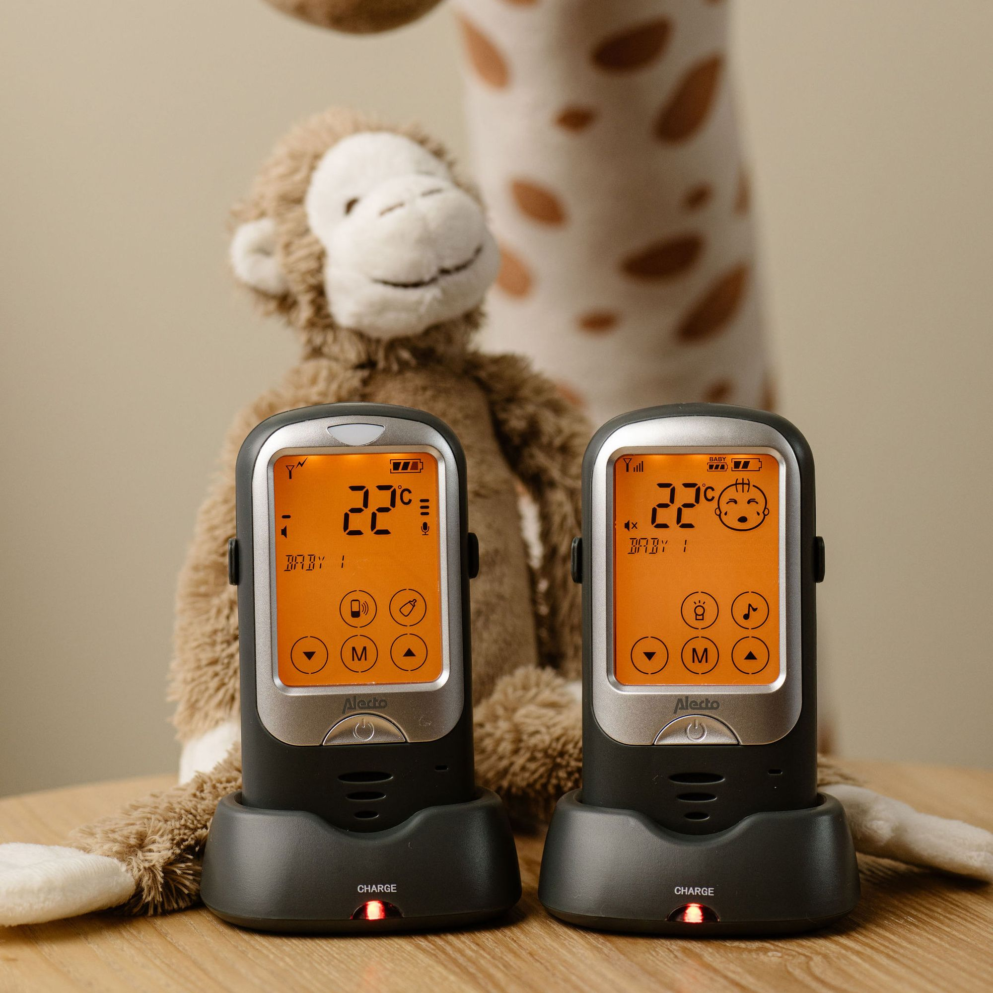 Deux babyphones sur une table en bois avec des peluches en arrière-plan.