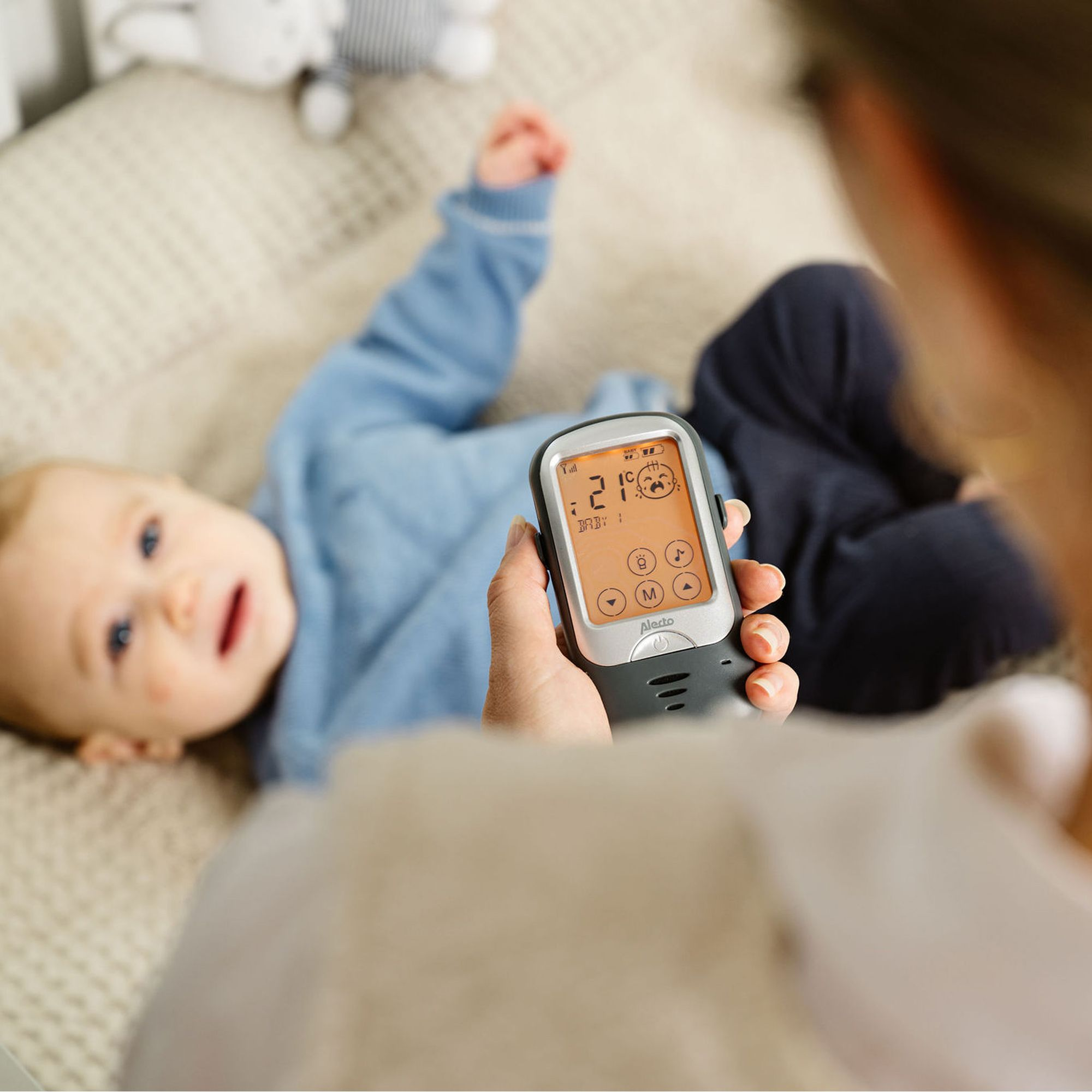 Babyphone zeigt 21 Grad an, Baby liegt auf dem Bett.