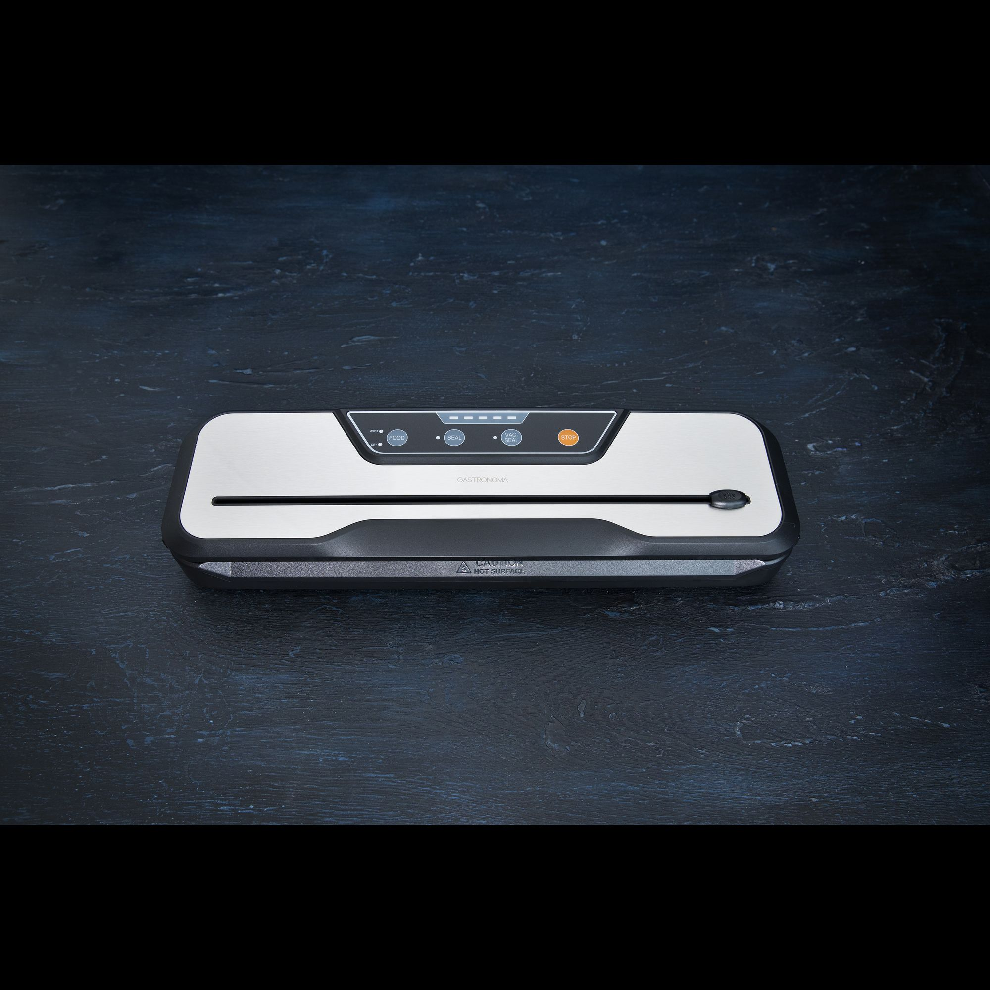 Srebrna zgrzewarka próżniowa z czarnymi detalami na ciemnym drewnianym stole.