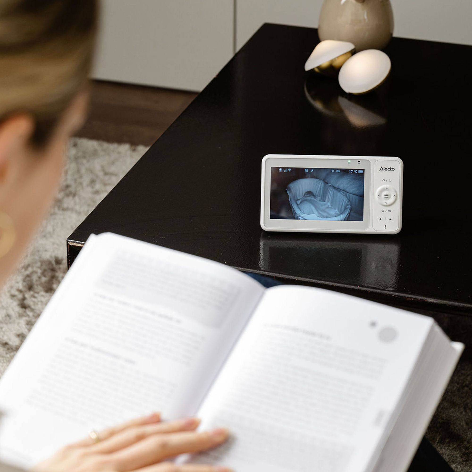 Kobieta czyta książkę, podczas gdy ekran niani elektronicznej pokazuje dziecko.
