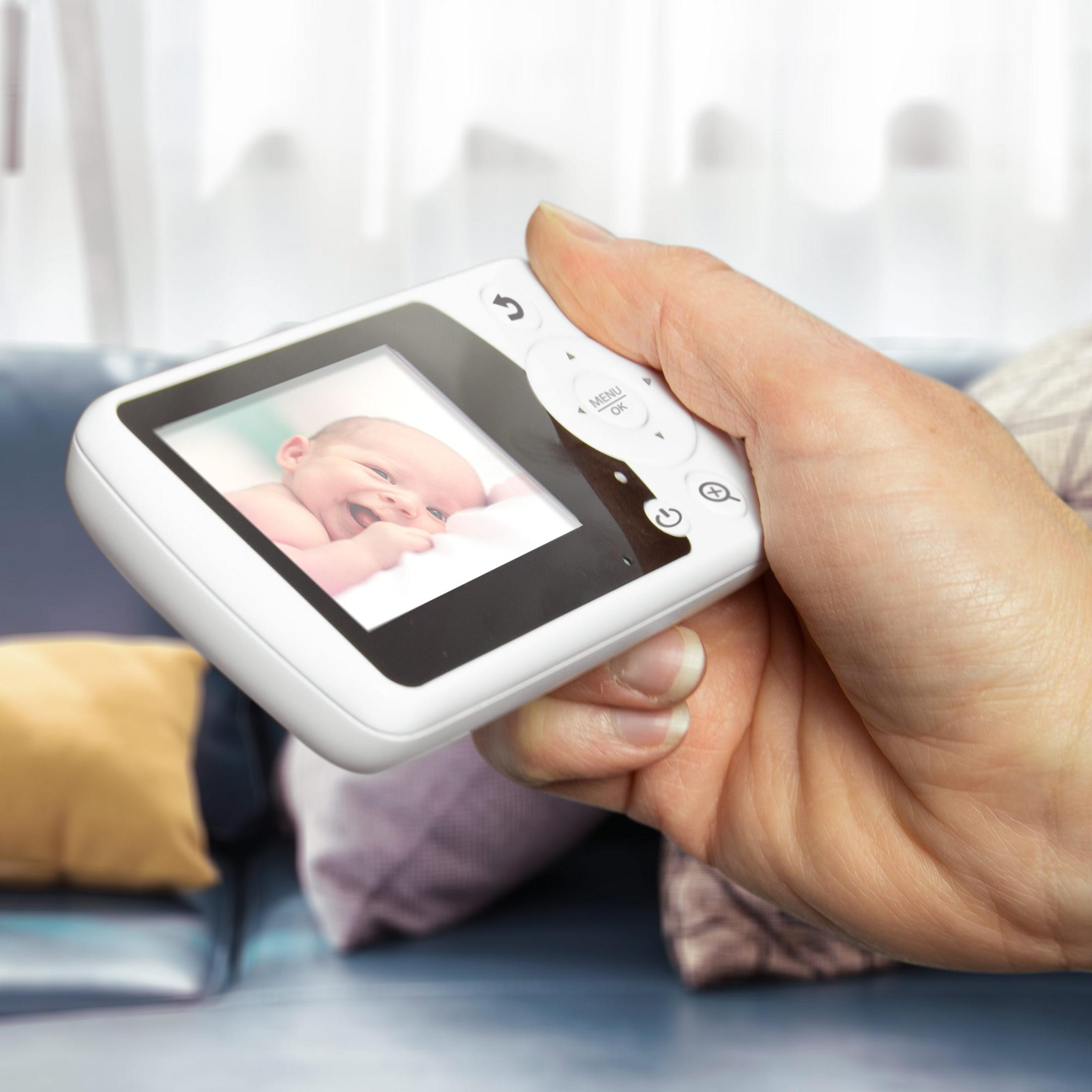 Dłoń trzyma biały monitor dla niemowląt pokazujący uśmiechnięte dziecko.