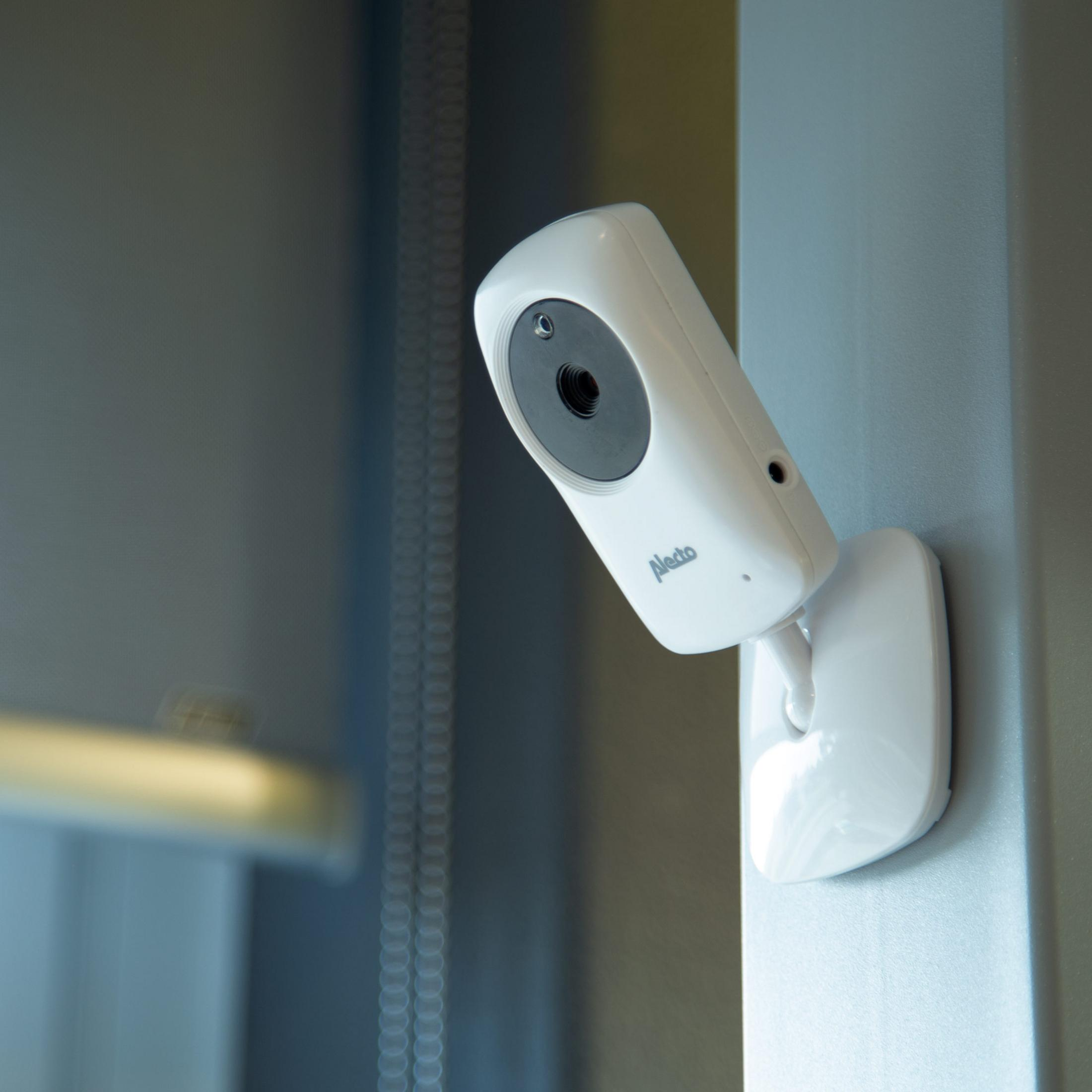 Biała kamera niani z obrotową głowicą jest zamontowana na ścianie.