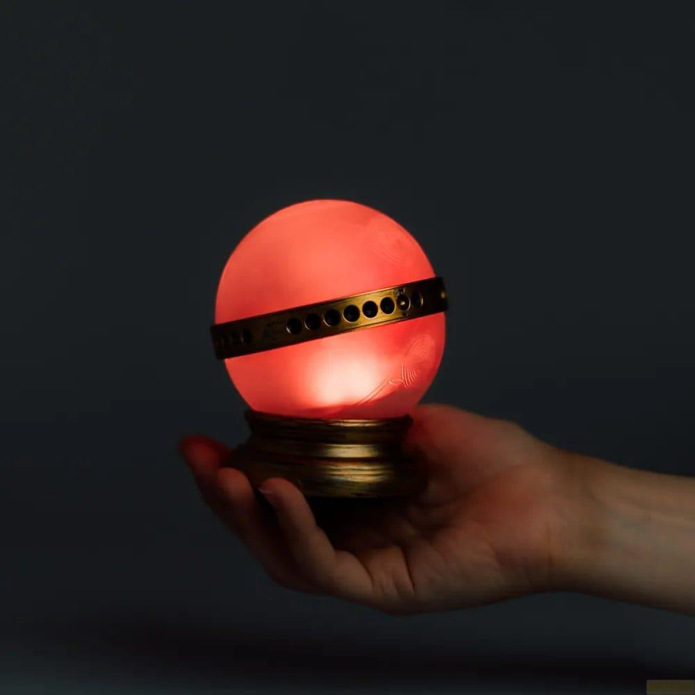 Una mano tiene un globo rosso luminoso su un supporto dorato.