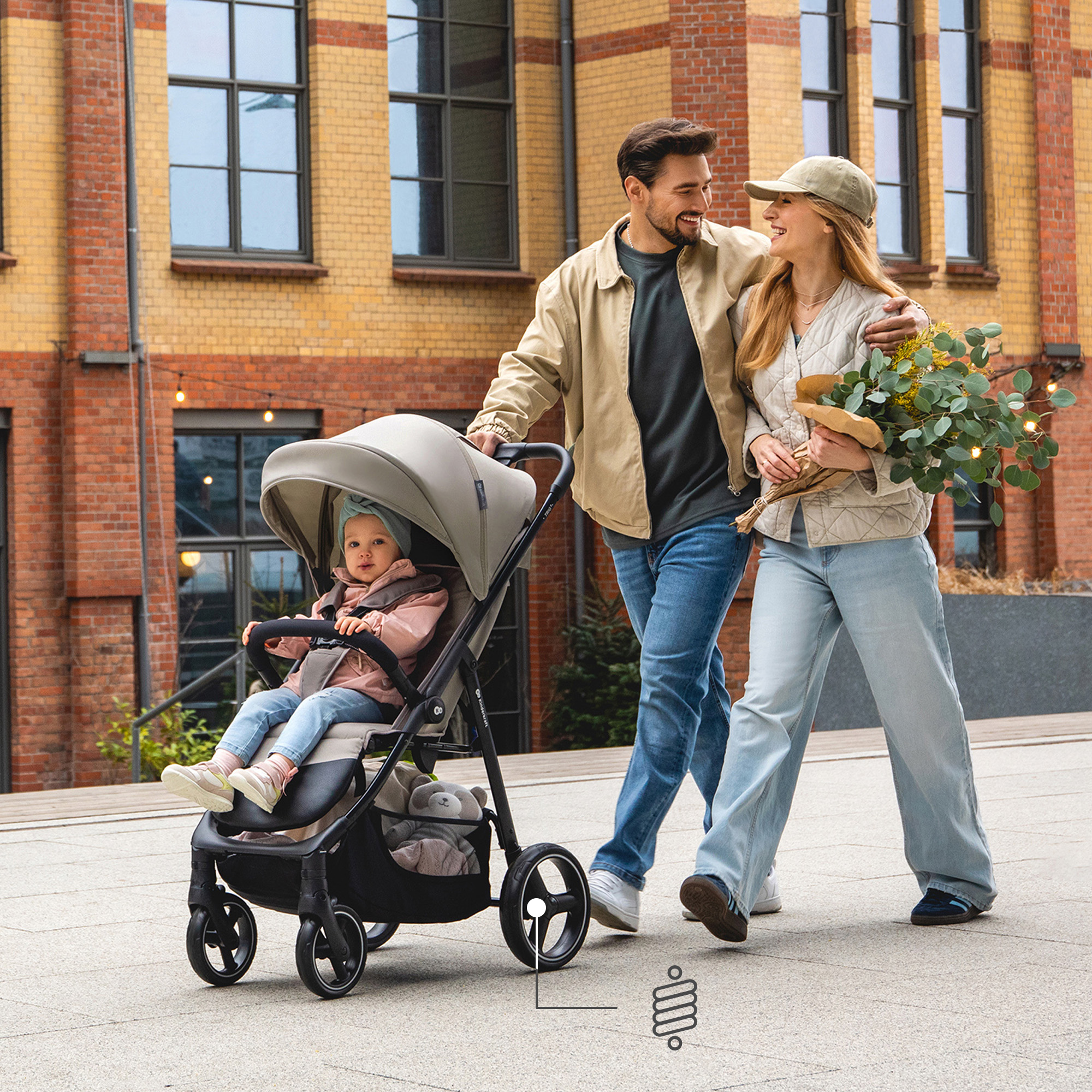 Ein Paar schiebt einen Kinderwagen mit Baby vor einem Backsteingebäude.