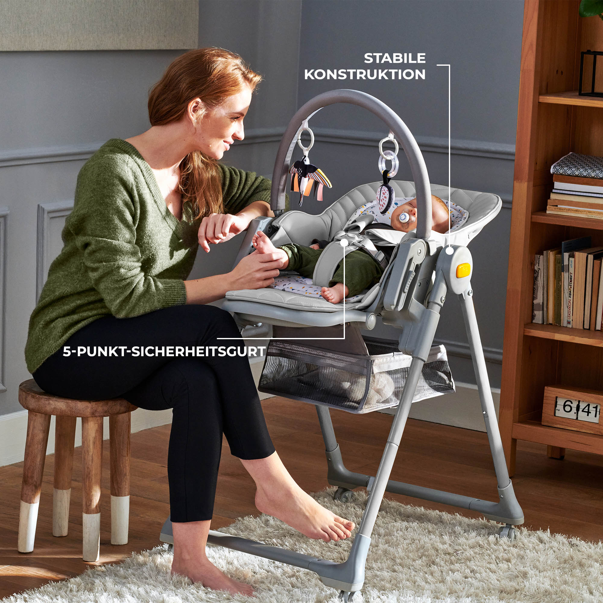 Eine Frau sitzt auf einem Hocker neben einem Babyhochstuhl mit einem Baby darin.