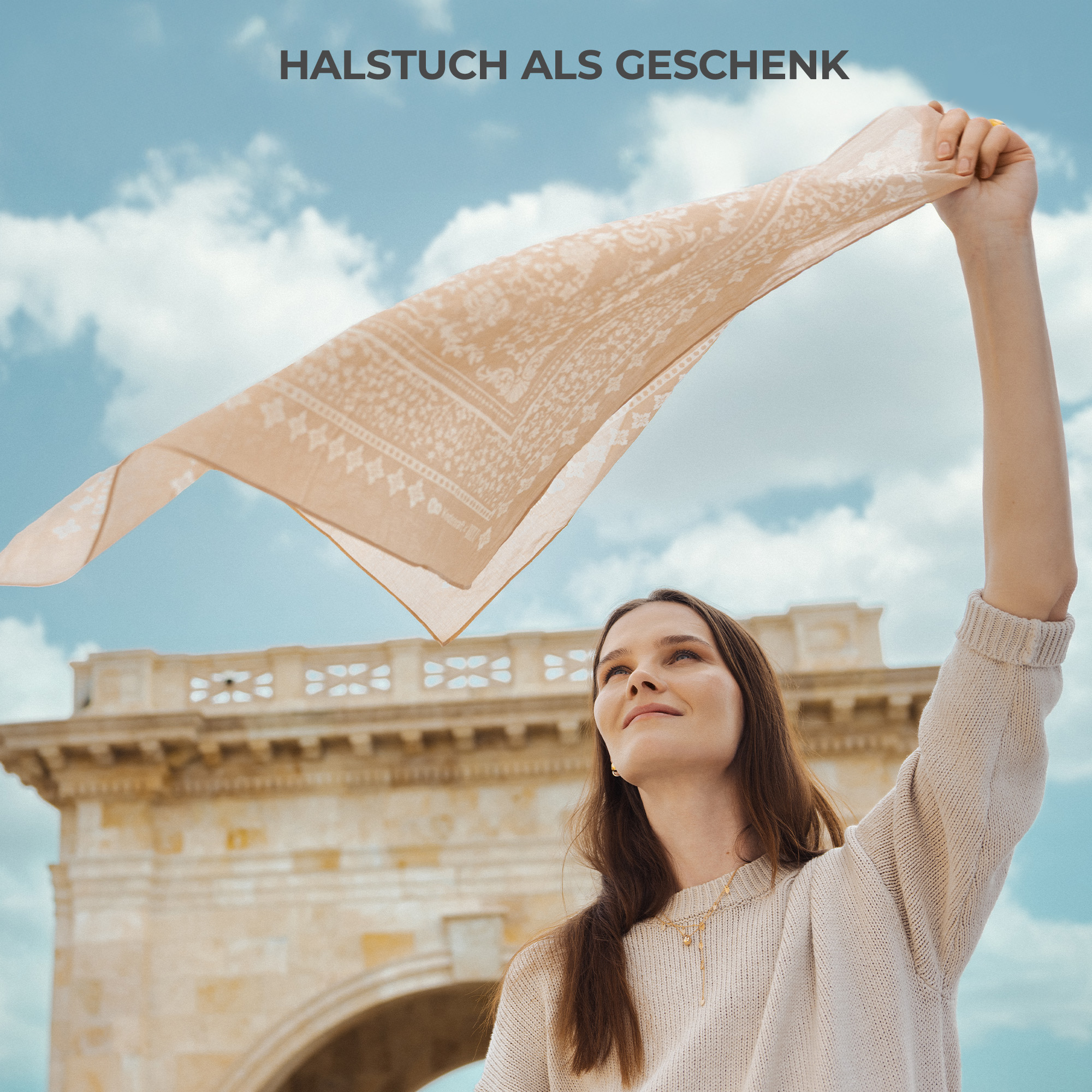 Frau mit beige Halstuch vor einer Steinarchitektur unter blauem Himmel.