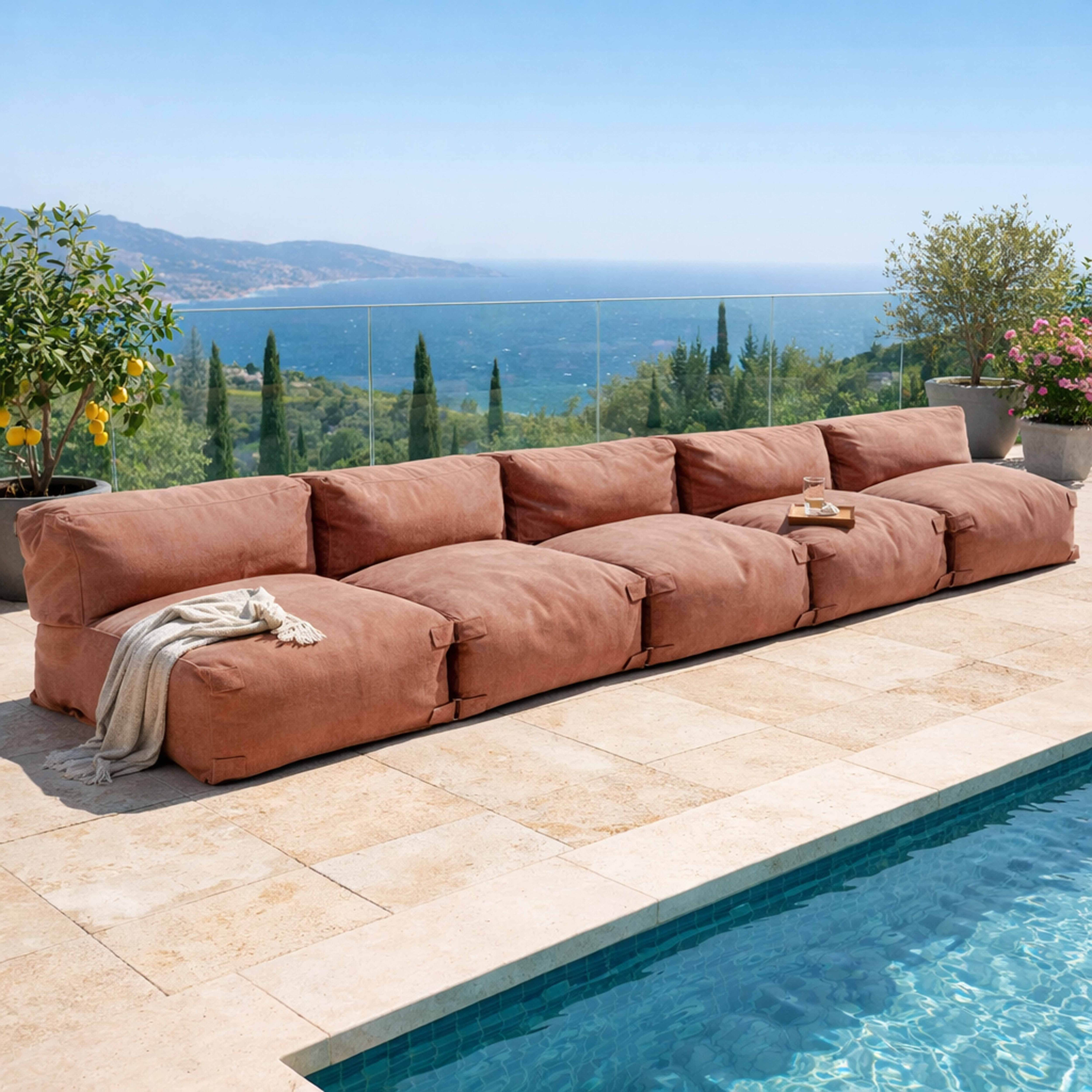 Eine lange, braune Couch steht am Pool mit Blick auf das Meer.
