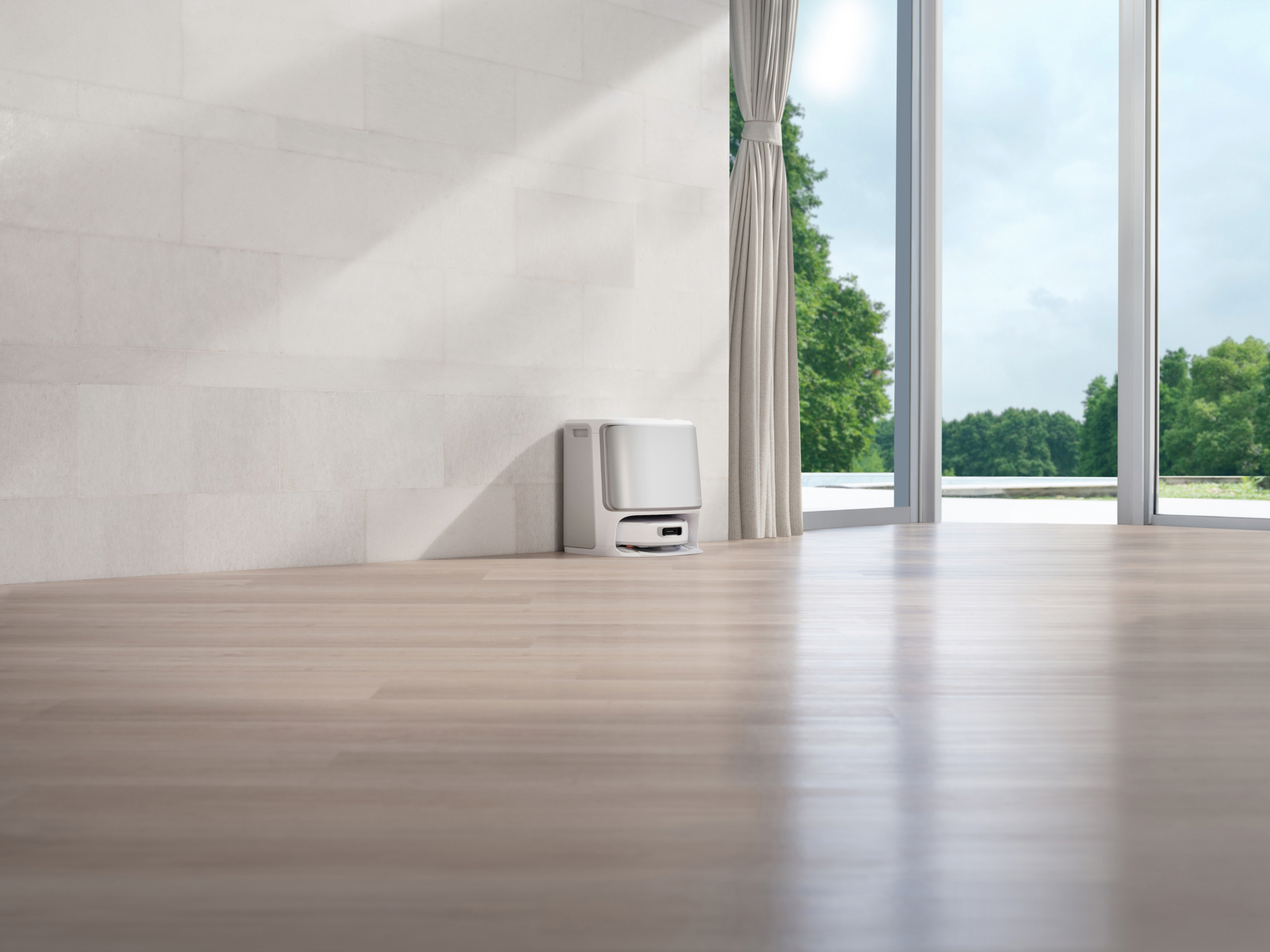 Een witte robotstofzuiger staat op een lichte houten vloer tegen een betegelde muur.
