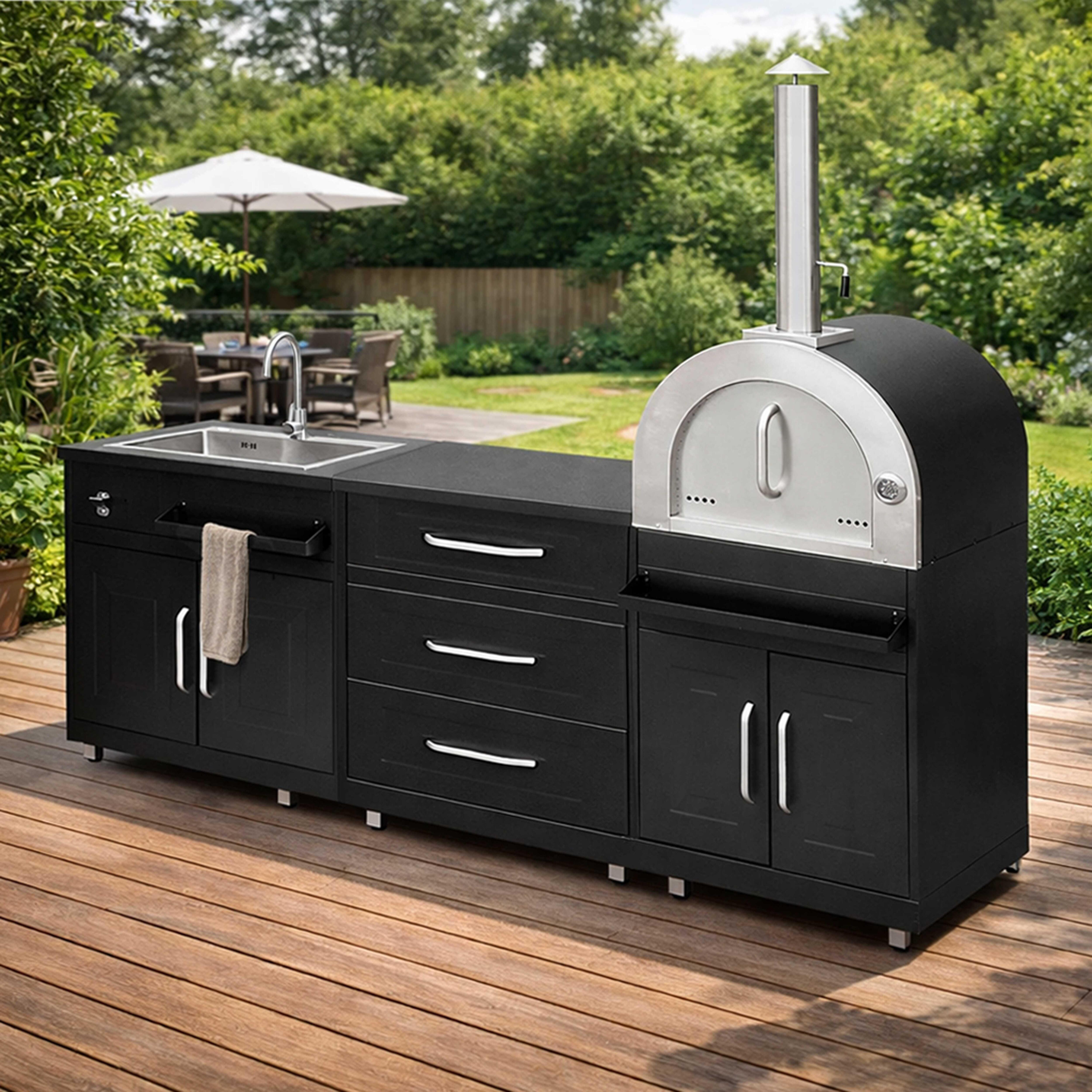 Schwarze Außenküche mit Spüle und Pizzaofen auf Holzdeck, Garten im Hintergrund.