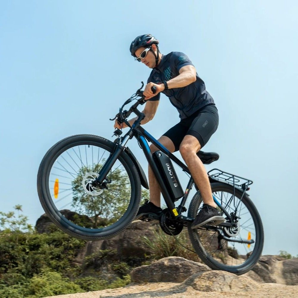 Hombre monta bicicleta eléctrica en terreno rocoso, rueda delantera en el aire.