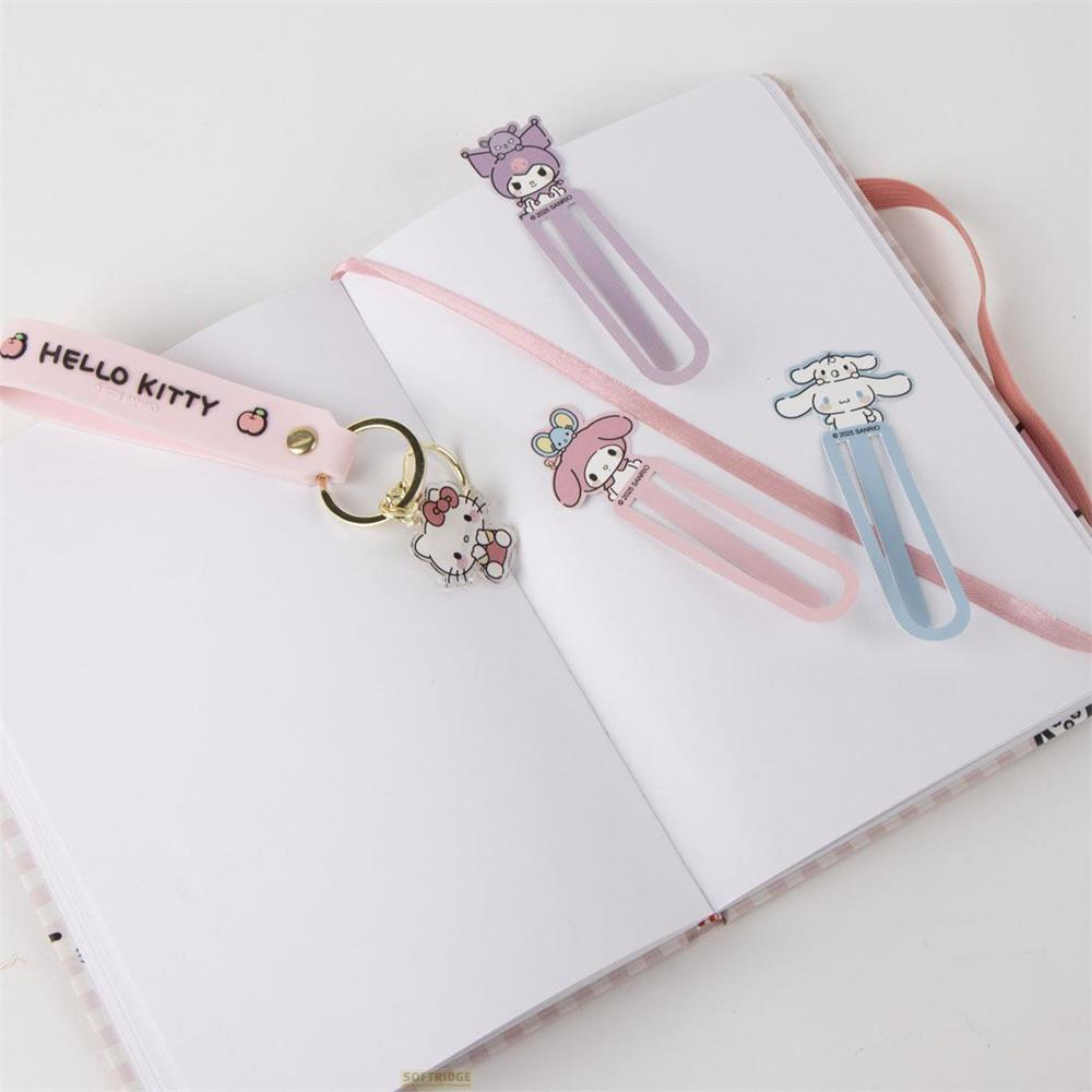 Un llavero rosa de Hello Kitty y tres marcapáginas de personajes Sanrio sobre un cuaderno abierto.